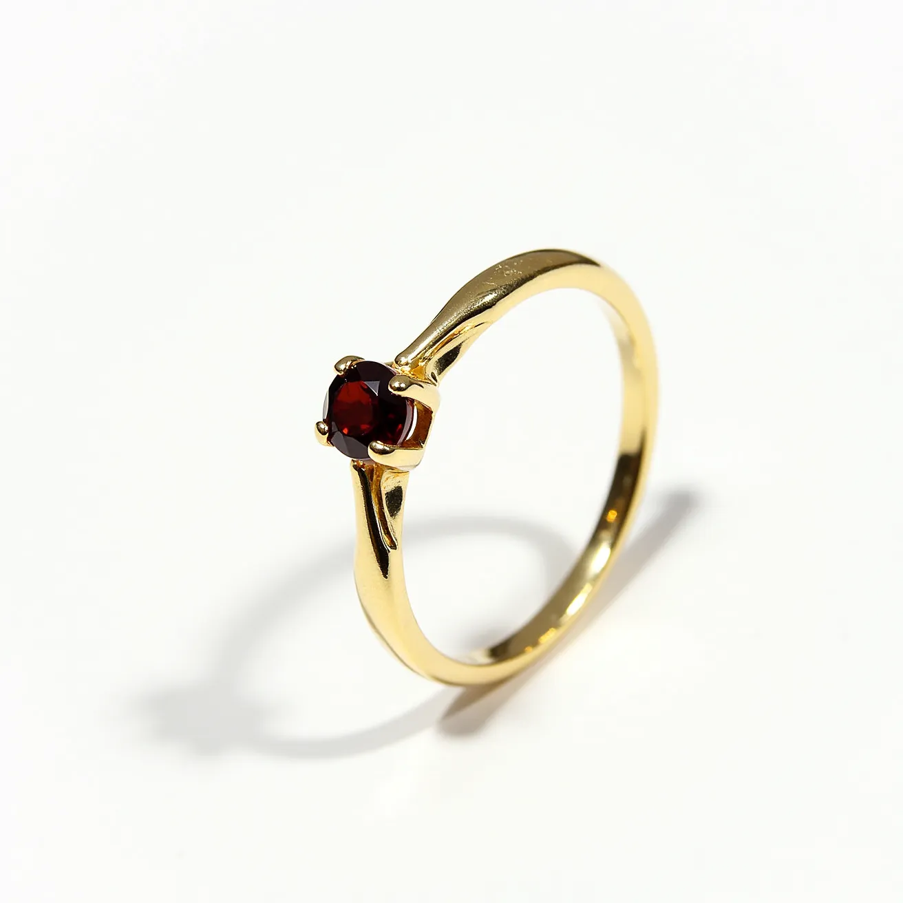 This garnet engagement ring features a deep red garnet as its central gemstone, expertly cut in a round shape to enhance its brilliance and depth. The garnet is set in a four-prong setting, which secures the stone while allowing light to pass through, enhancing its vibrant color. The band is crafted from a polished yellow metal, likely gold, providing a warm and classic contrast to the bold red of the garnet. The simple yet elegant setting highlights the beauty of the garnet, making it the focal point of the ring.