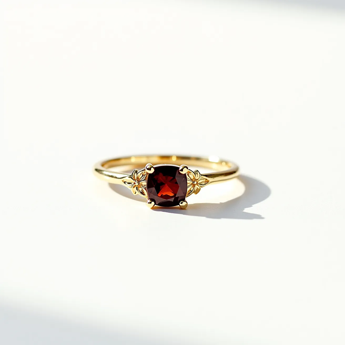 This garnet engagement ring features a striking deep red garnet as its centerpiece, cut in a cushion shape that highlights the stone's rich color and clarity. The garnet is securely set in a claw setting, allowing maximum visibility of the gemstone. The band is crafted from a lustrous gold material, providing a warm and elegant backdrop that enhances the garnet's fiery hue. The sides of the ring are adorned with intricate gold designs that add sophistication and charm to the piece. The combination of the garnet's vibrant color and the gold's opulent finish creates a timeless and elegant piece of jewelry.