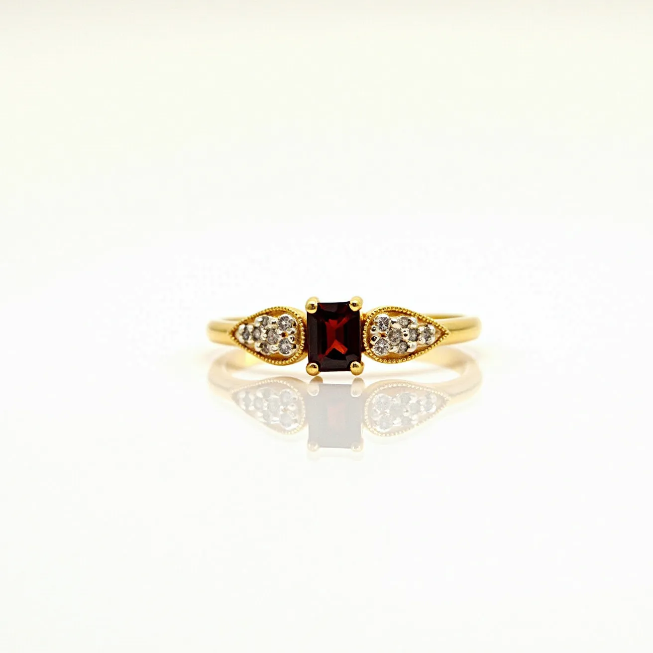 This garnet ring features a deep red garnet stone at its center, precisely cut in a rectangular shape, set in a gold band. The garnet is secured with a classic four-prong setting, giving it an elegant and elevated appearance. Flanking the central stone are pear-shaped clusters of smaller, sparkling clear stones, likely diamonds or cubic zirconia, which are also set into the gold band, creating a sophisticated contrast. The smooth, polished gold band enhances the overall luxurious feel, ensuring the gemstones remain the focal point of the piece.