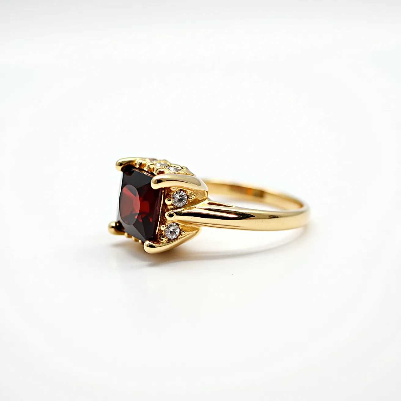 This garnet ring features a striking deep red garnet as its centerpiece, showcased in a sophisticated cushion cut that enhances its rich color and brilliance. The garnet is securely set in a prong setting, which allows maximum light to enter the stone from multiple angles, further enhancing its vividness. The band of the ring is crafted from polished yellow gold, adding a warm and luxurious contrast to the deep hue of the garnet. Flanking the central gem are smaller round diamonds set on either side, adding a touch of sparkle and elegance to the piece. The combination of gemstones and precious metal creates a harmonious and opulent design, making it a standout accessory.