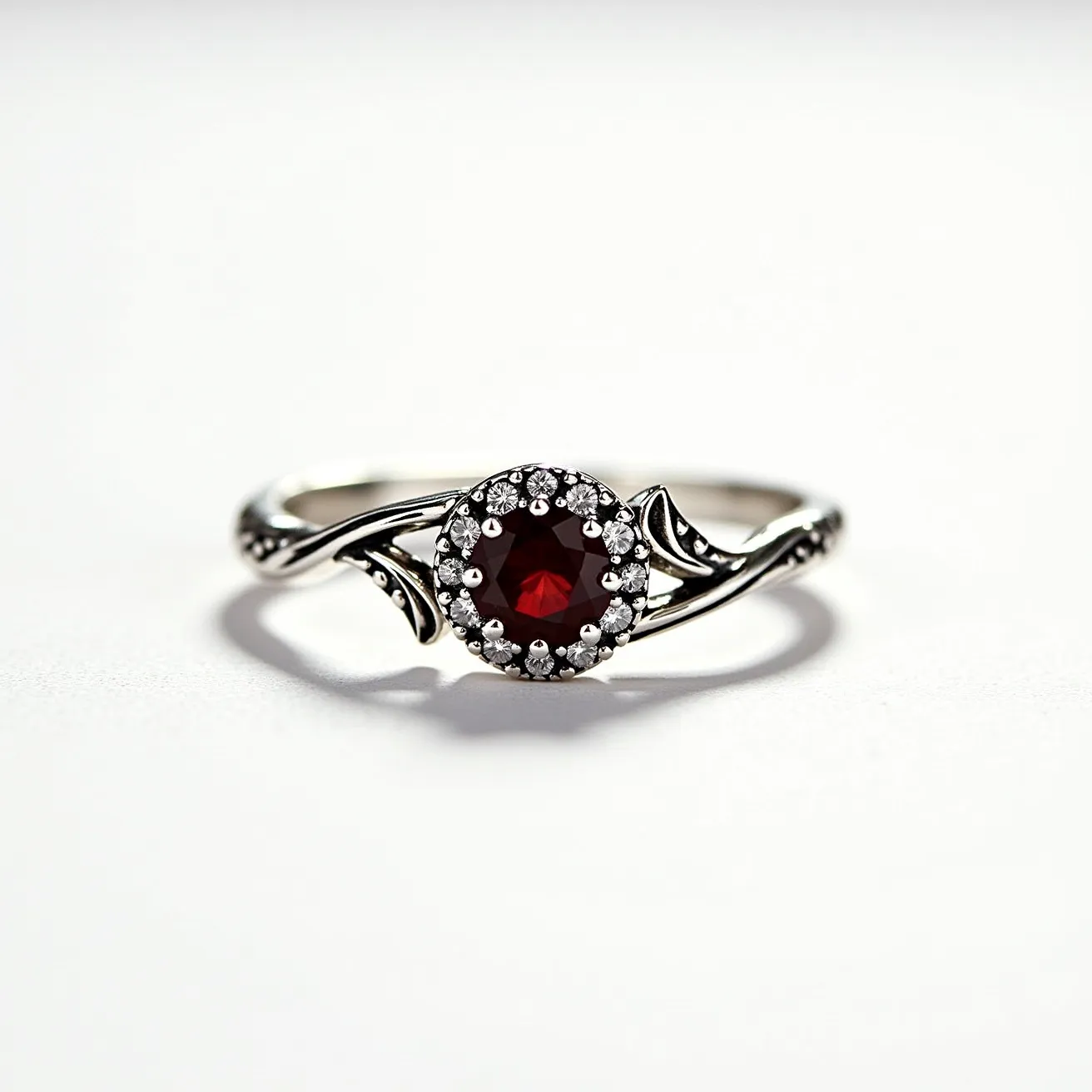 This garnet wedding ring features a central, round-cut garnet gemstone, richly hued in a deep red color. The garnet is surrounded by a halo of small, sparkling diamonds which enhance its brilliance and create a stunning contrast. The setting appears to be crafted from white gold, showcasing intricate, flowing designs that add an artistic touch to the band. The overall composition of the ring marries elegance with a vintage-inspired aesthetic, making it a unique choice for a wedding band.