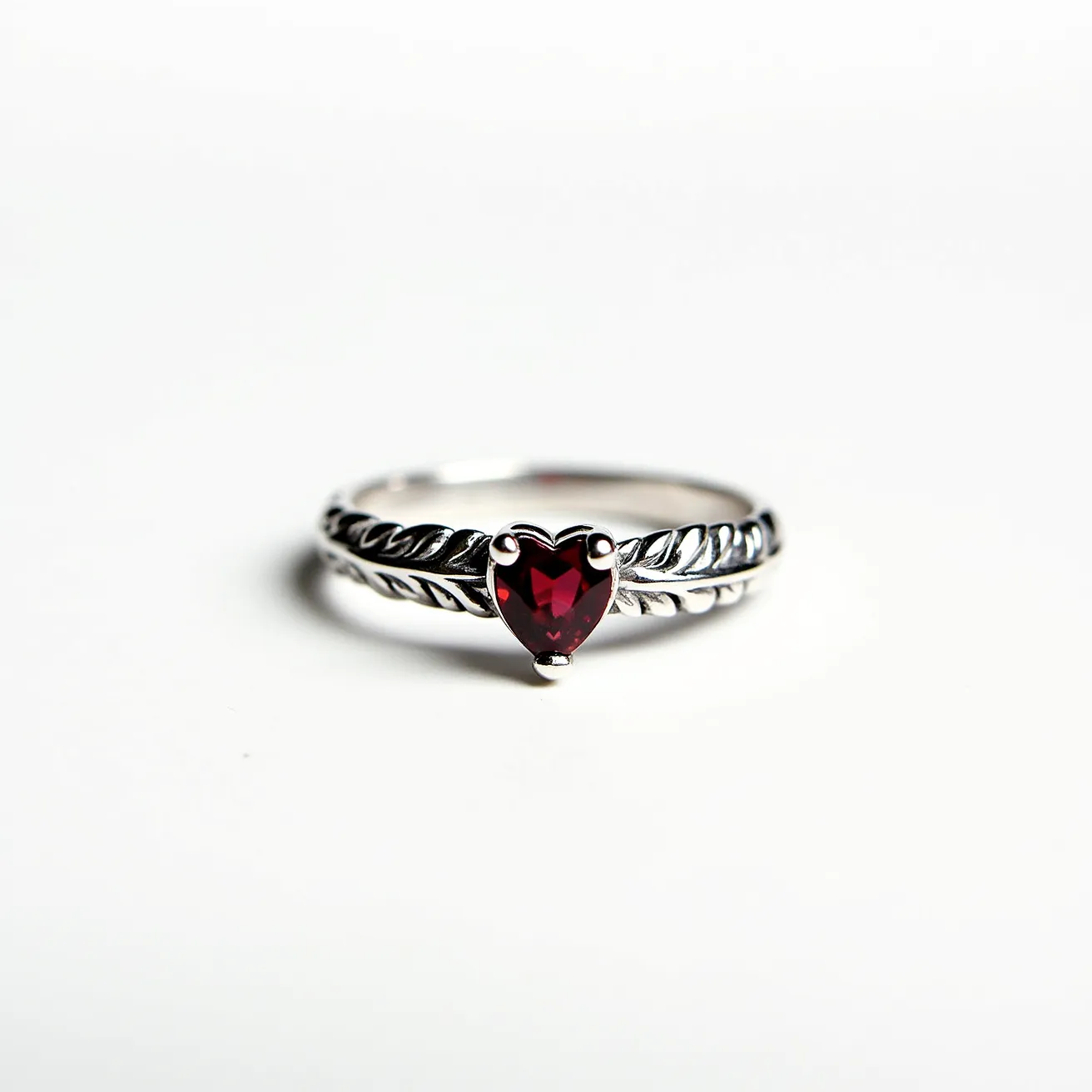 This garnet wedding ring features a heart-shaped garnet gemstone prominently set in a prong setting, which securely holds the stone in place. The band is made of metal, likely white gold or sterling silver, and is adorned with an intricate leaf pattern that adds a touch of elegance and sophistication to the overall design. The prong setting ensures that the garnet is the focal point of the ring, highlighting its deep red hue and unique cut. The craftsmanship of the band complements the rich color of the garnet, making this ring a striking piece of jewelry.