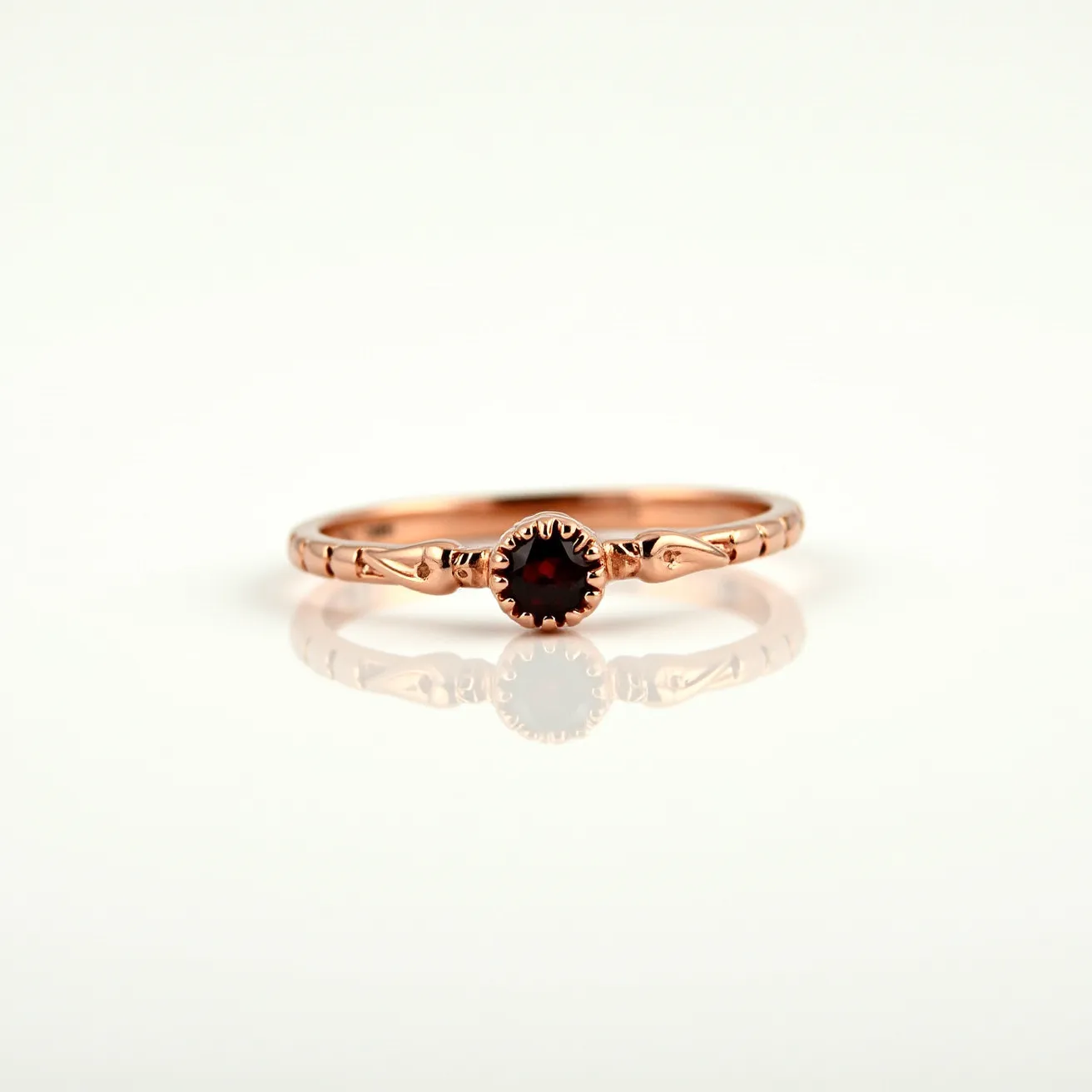 This garnet wedding ring features a sleek, rose gold band with a delicately intricate design that enhances its elegance. At the center, a round-cut garnet gemstone is securely held by a bezel setting, showcasing its rich, deep red hue. The band bears subtle embellishments that contribute to its refined appearance. The combination of the warm rose gold and the vivid garnet creates a harmonious and romantic aesthetic, making this ring a striking symbol of love and commitment.