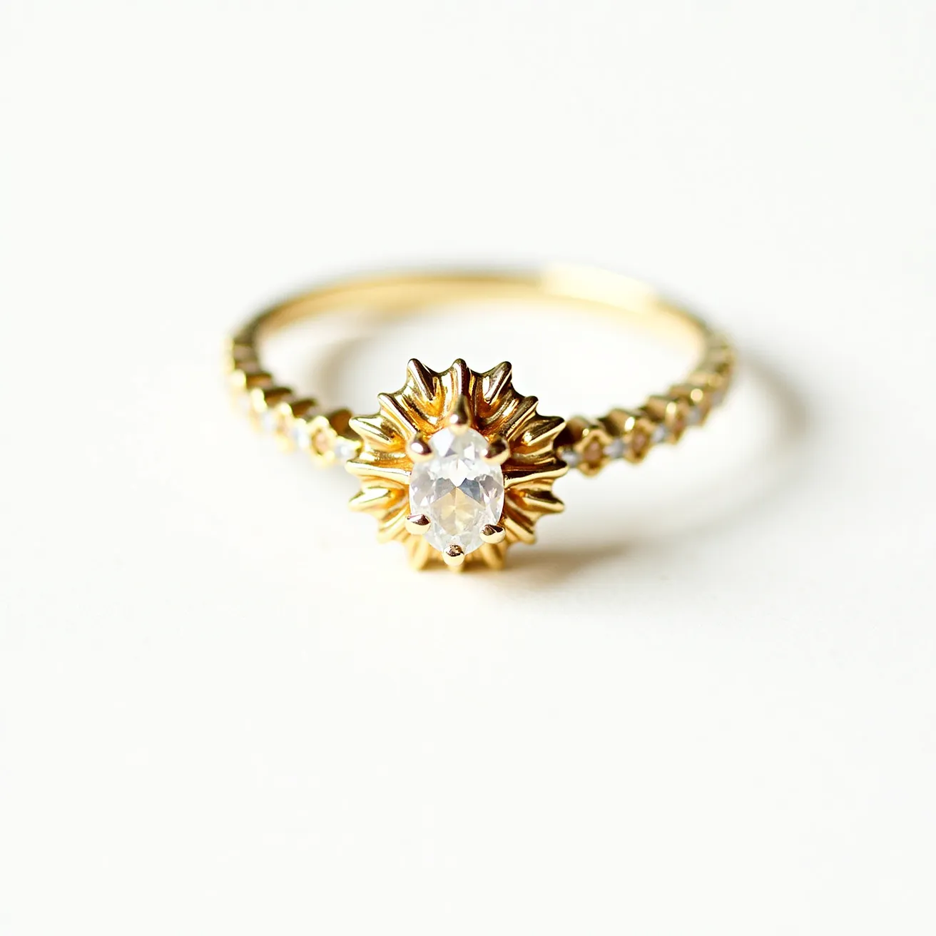 This gemstone engagement ring features a centerpiece oval-cut clear gemstone set in a unique sunburst design. The band is crafted from gold, showcasing intricate detailing that emphasizes its elegance. Small round gems are embedded along the band, adding to the ring's sparkle and allure. The central stone is securely held in place by a prong setting, ensuring durability and prominence against the ornate design of the gold band.