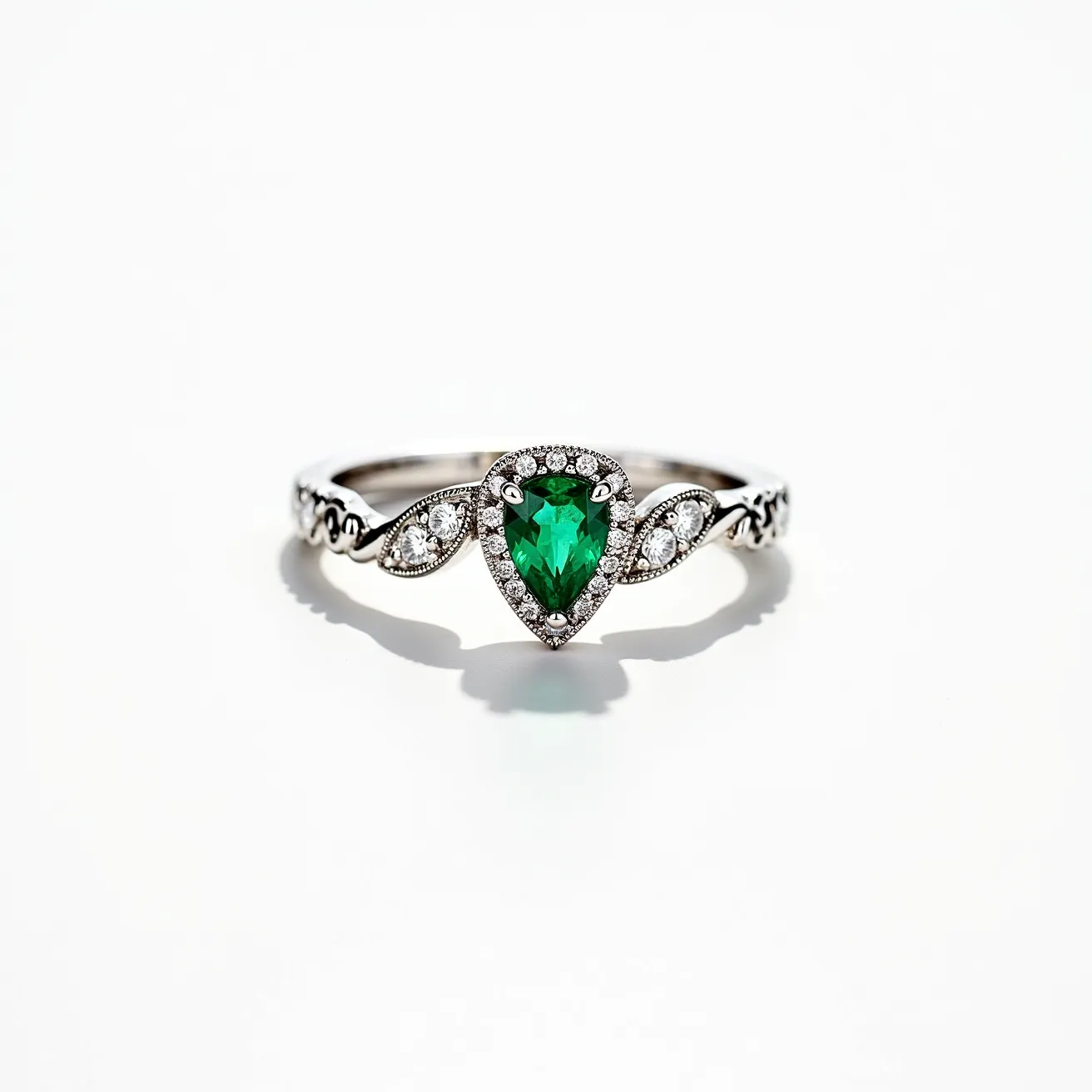 This gemstone engagement ring features a stunning pear-cut emerald as the centerpiece, surrounded by a halo of small round diamonds that enhance its vibrancy and brilliance. The emerald is securely set in a polished white metal, likely platinum or white gold, giving the ring a sleek and elegant appearance. Flanking the central emerald are two marquise-shaped settings, each holding small round diamonds, which are seamlessly integrated into the band’s design, adding to its intricate beauty. The band itself is adorned with delicate metalwork, continuing the luxurious and sophisticated aesthetic.