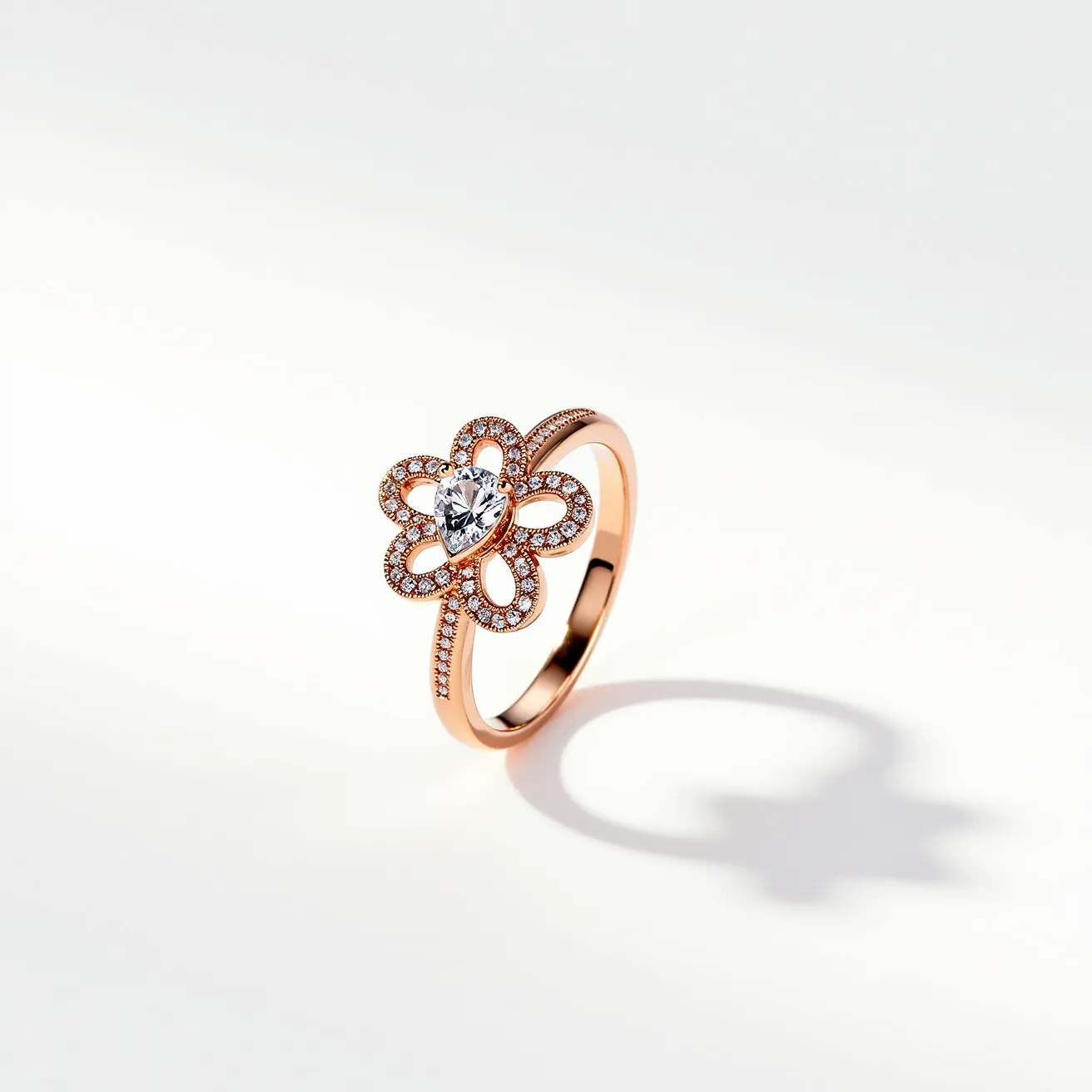 This gemstone ring showcases a rose gold band adorned with a charming floral design, featuring a prominent pear-shaped diamond at its center. Surrounding the central stone, intricate loops of smaller round-cut diamonds enhance the petal motif, adding brilliance and elegance. The sleek band, also lined with tiny diamonds, complements the sophisticated setting of the main gems, creating a harmonious blend of luxury and style. The ring is elegantly crafted to provide both beauty and comfort, making it a stunning piece of jewelry.