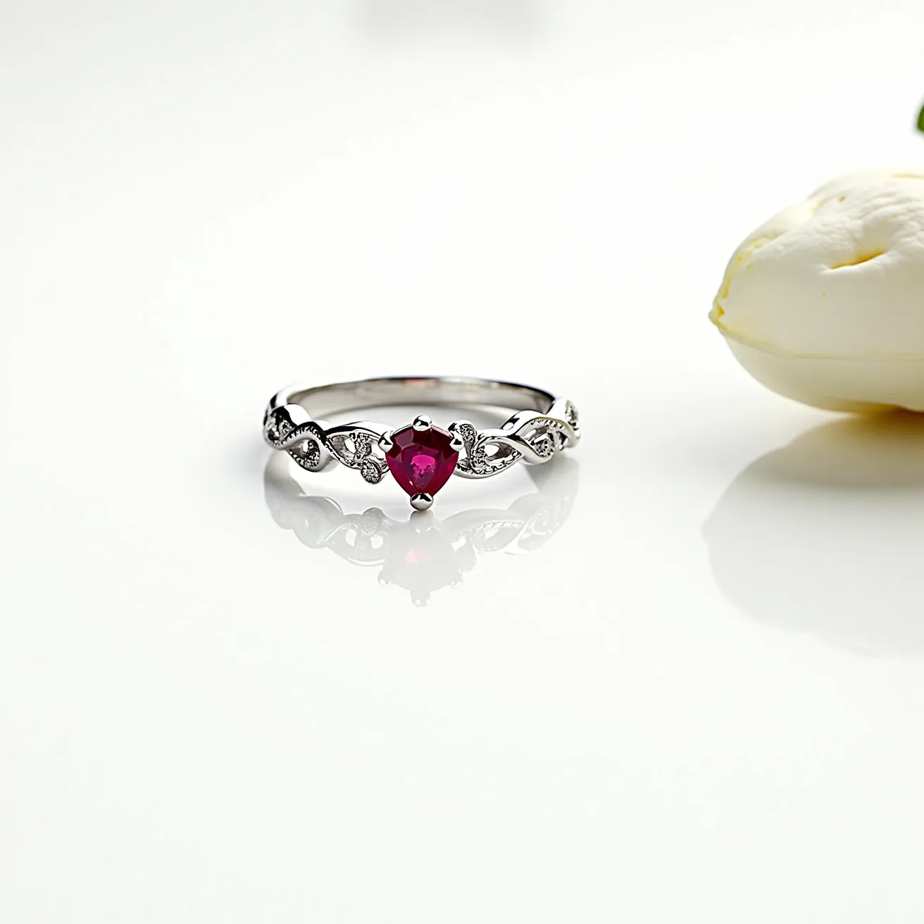 This gemstone ring features a striking heart-shaped red stone, likely a ruby, set in a secure claw setting at its center. The band is crafted from silver or white gold, offering a sleek and polished appearance. Delicate leaf-like patterns embellished with small, round gems, potentially diamonds or cubic zirconia, are interspersed along the band, enhancing the ring’s elegant design. The metal band and its intricate detailing contribute to the piece's graceful and sophisticated aesthetic, ideal for special occasions.