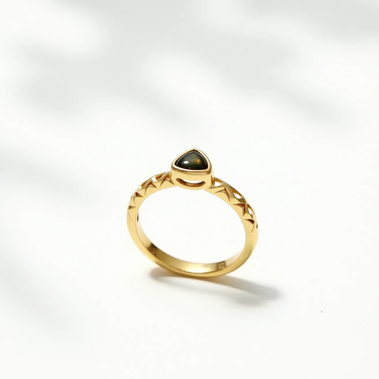 This gemstone ring features a beautifully set dark stone with a smooth, rounded surface, suggesting a cabochon cut, positioned at the top in a bezel setting. The ring is crafted from gold, evident from its yellow metallic luster, which also adorns the band with an intricate pattern of geometric cutouts along its sides. The overall design is elegant and minimalist, with a focus on highlighting the unique shape and hue of the gemstone. The ring does not include any visible clasps or additional attachments, emphasizing its streamlined and classic style.