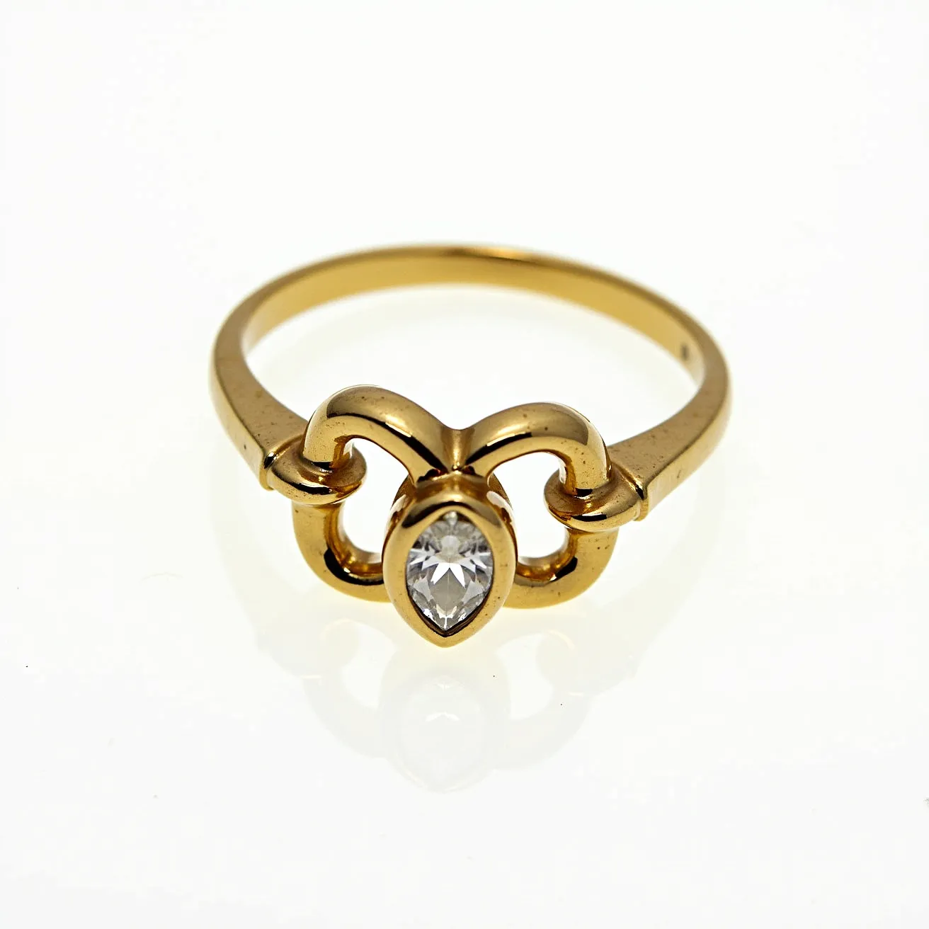 This gold ring features a pear-cut gemstone set at its center, held securely within a bezel setting. The band is crafted from gold, with a smooth and polished appearance that complements the simplistic yet elegant design. The central gem, likely a diamond or diamond-like stone, adds a striking focal point to the piece. The design incorporates a symmetrical pattern that elegantly frames and accentuates the beauty of the center stone. There are no additional clasps or attachments, allowing the ring to maintain its refined and seamless aesthetic.