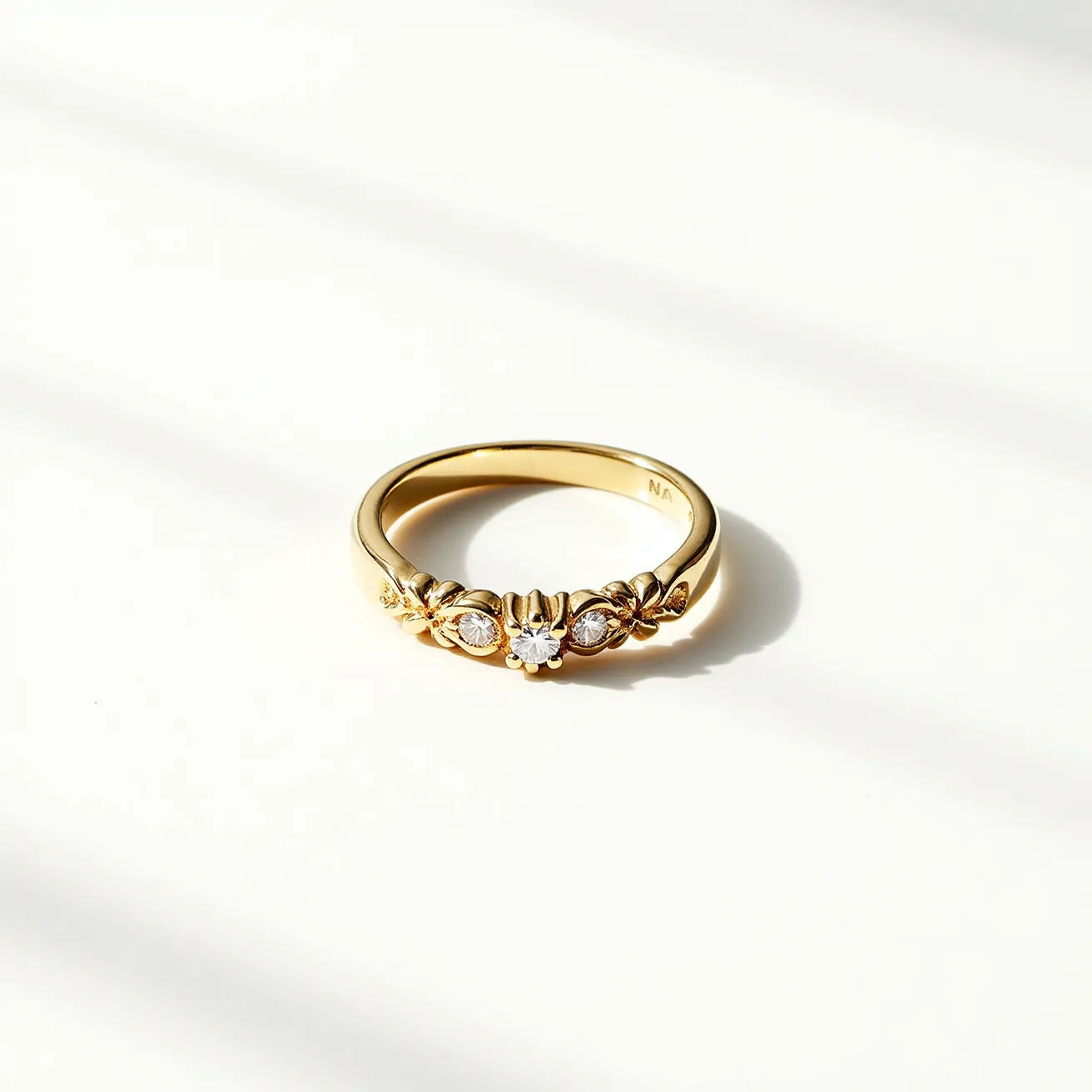 This gold ring features a polished band and is adorned with three gemstones. The central stone is a round-cut gem, complemented by two smaller round stones on either side. These stones are set in a detailed claw setting that enhances their brilliance. The design incorporates decorative elements around the settings that add elegance to the overall aesthetic. The ring does not include any additional clasps or attachments, maintaining a classic and sophisticated look.