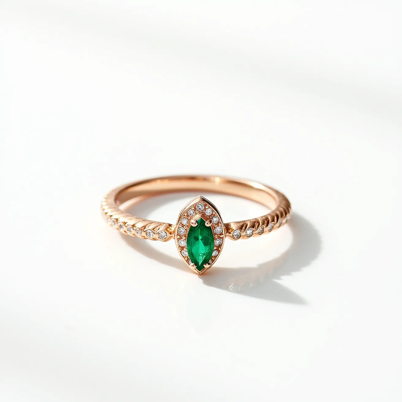 This gold ring features a marquise-cut green gemstone, likely an emerald, set at its center. The centerpiece is surrounded by a halo of small round clear stones, possibly diamonds, enhancing its brilliance. The band itself is crafted from gold and has a twisted design, adorned with equally spaced small clear stones, matching those in the halo. The setting and overall design give the ring an elegant and sophisticated appearance, with no visible clasp or attachment, suggesting a traditional circular shape.