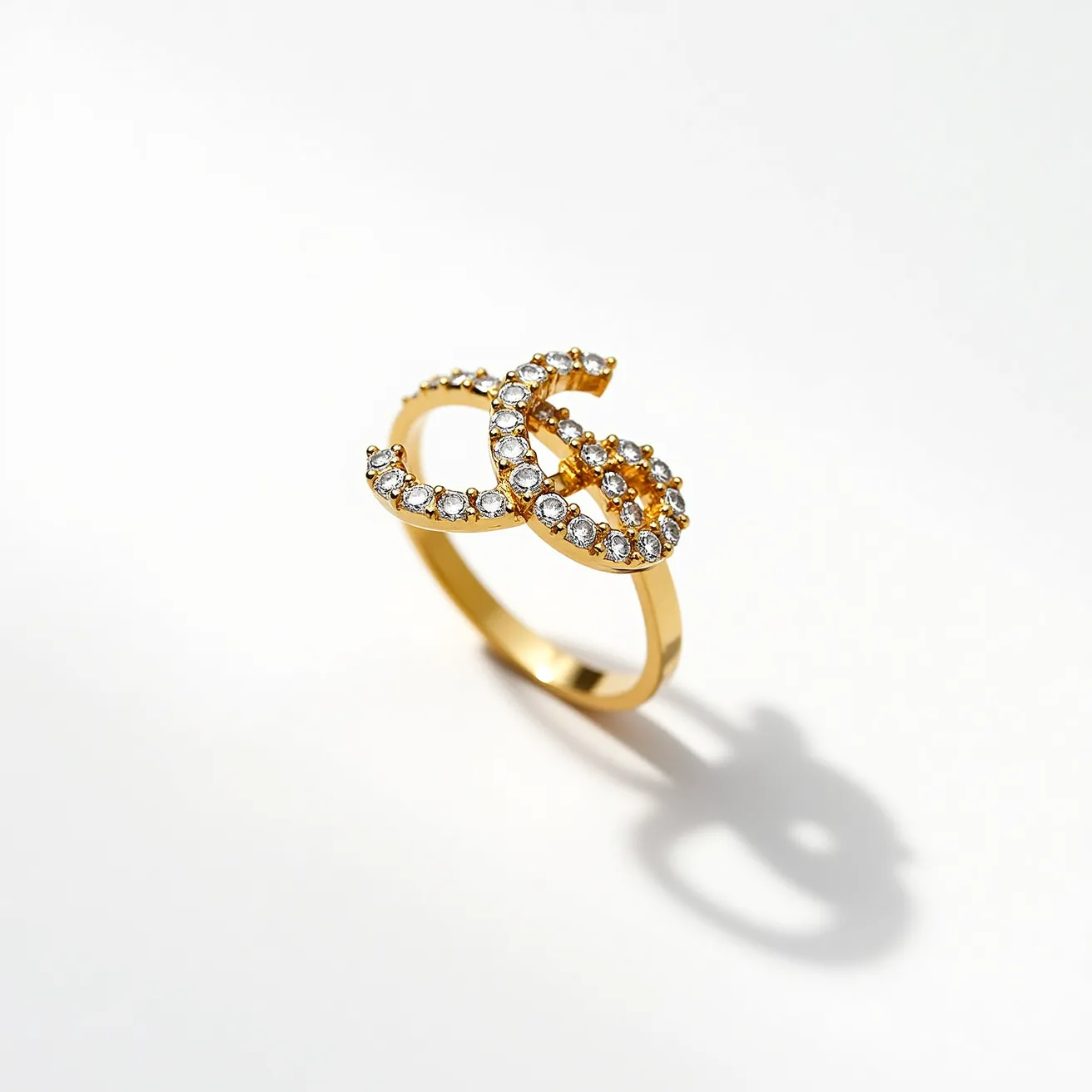 This gold thumb ring features a band crafted from a lustrous gold material. The focal point of the ring is an interlocking design, embellished with numerous small, round-cut clear stones that resemble diamonds. These stones are set in a pavé setting, providing a continuous shimmer across the surface. The overall design exhibits an elegant and intricate appearance, with the stones securely held in place by the metal prongs, enhancing the ring's visual appeal without the need for additional clasps or attachments.