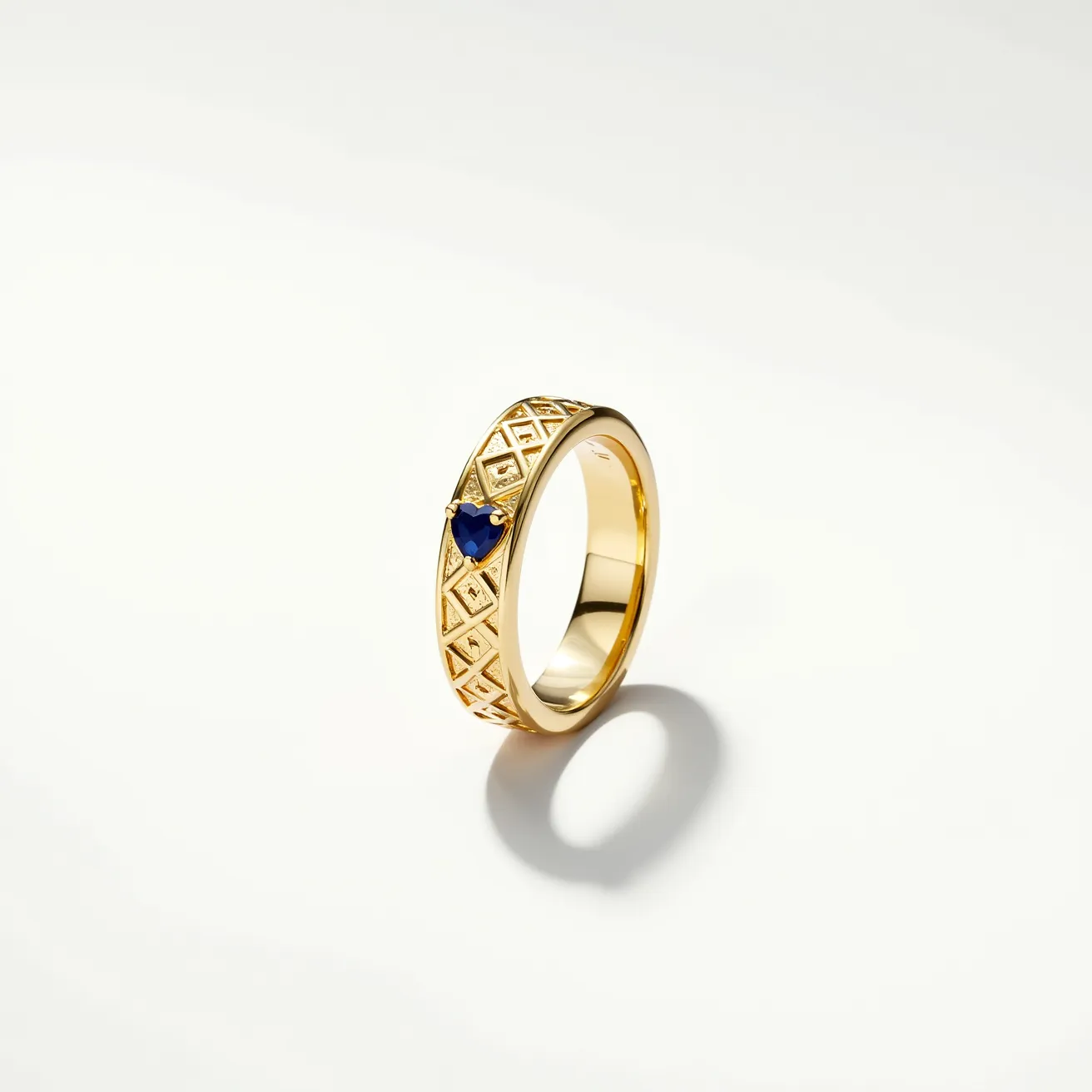 This gold wedding band features an intricate design with geometric patterns that add a touch of sophistication to its appearance. The band is adorned with a prominent blue gemstone, likely a sapphire, which is heart-shaped and set in a secure prong setting, adding a pop of color to the design. The smooth inner band suggests comfort for the wearer, while the outer details highlight craftsmanship and style. The gold material gives the ring both a classic and timeless look, making it a beautiful piece of jewelry.