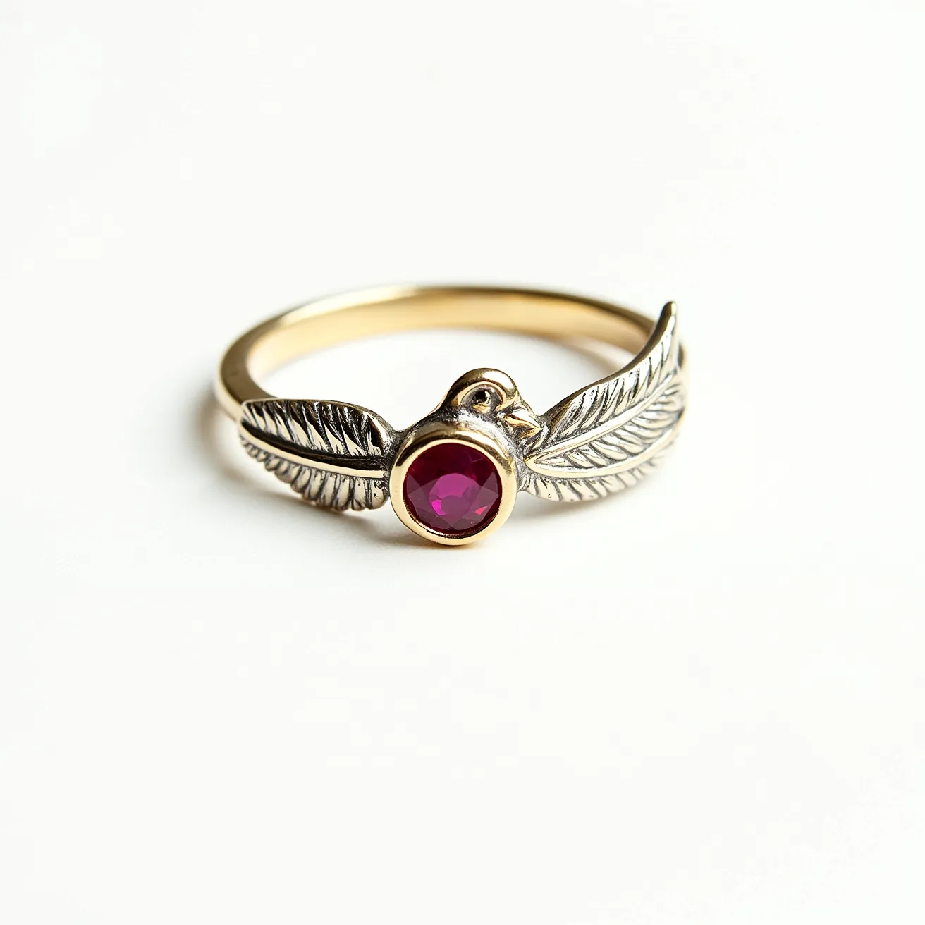 This golden bird ring features an intricately designed bird motif, with its wings elegantly wrapping around the band. The ring is primarily crafted from gold, showcasing a lustrous finish that enhances its luxurious appeal. At the center, a round-cut, vibrant red gemstone, possibly a ruby, is set in a bezel setting, securely nestled between the bird's head and wings. The detailed textures on the wings add a refined touch to the overall design, and there is no visible clasp or attachment, indicating it is meant to be a slip-on ring.