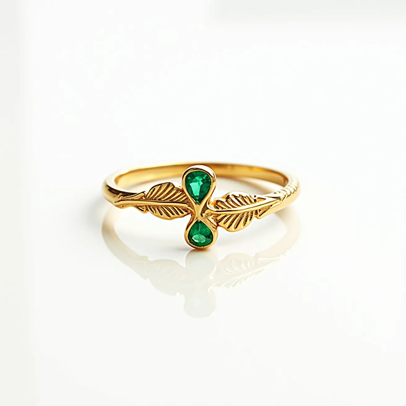 This golden bird ring features a delicate design crafted from gold, showcasing two intricately detailed wings. The centerpiece of the ring includes two small, pear-shaped, deep green gemstones, which are likely emeralds, each set at the widest part of the band and oriented with their points facing each other. The gems are bezel-set, offering a secure hold while enhancing the ring's elegant aesthetic. The overall design combines the rich color of the gemstones with the polished luster of the gold, creating a harmonious and refined look.