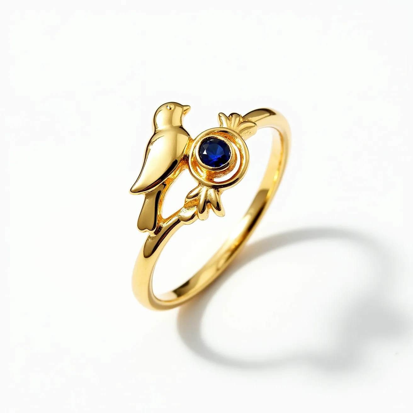 This golden bird ring showcases a delicate design, featuring a bird motif perched beside a circular setting. The ring is crafted from a polished gold material, which gives it a luxurious shine. At the center of the design is a stunning blue gemstone, likely a sapphire, cut in a round shape and securely set within a bezel setting. The smooth contours of the ring highlight the elegance of both the metal and the gemstone, creating a harmonious balance between the two elements. The band itself is sleek and simple, allowing the intricate details of the bird and gemstone to stand out as the focal points.