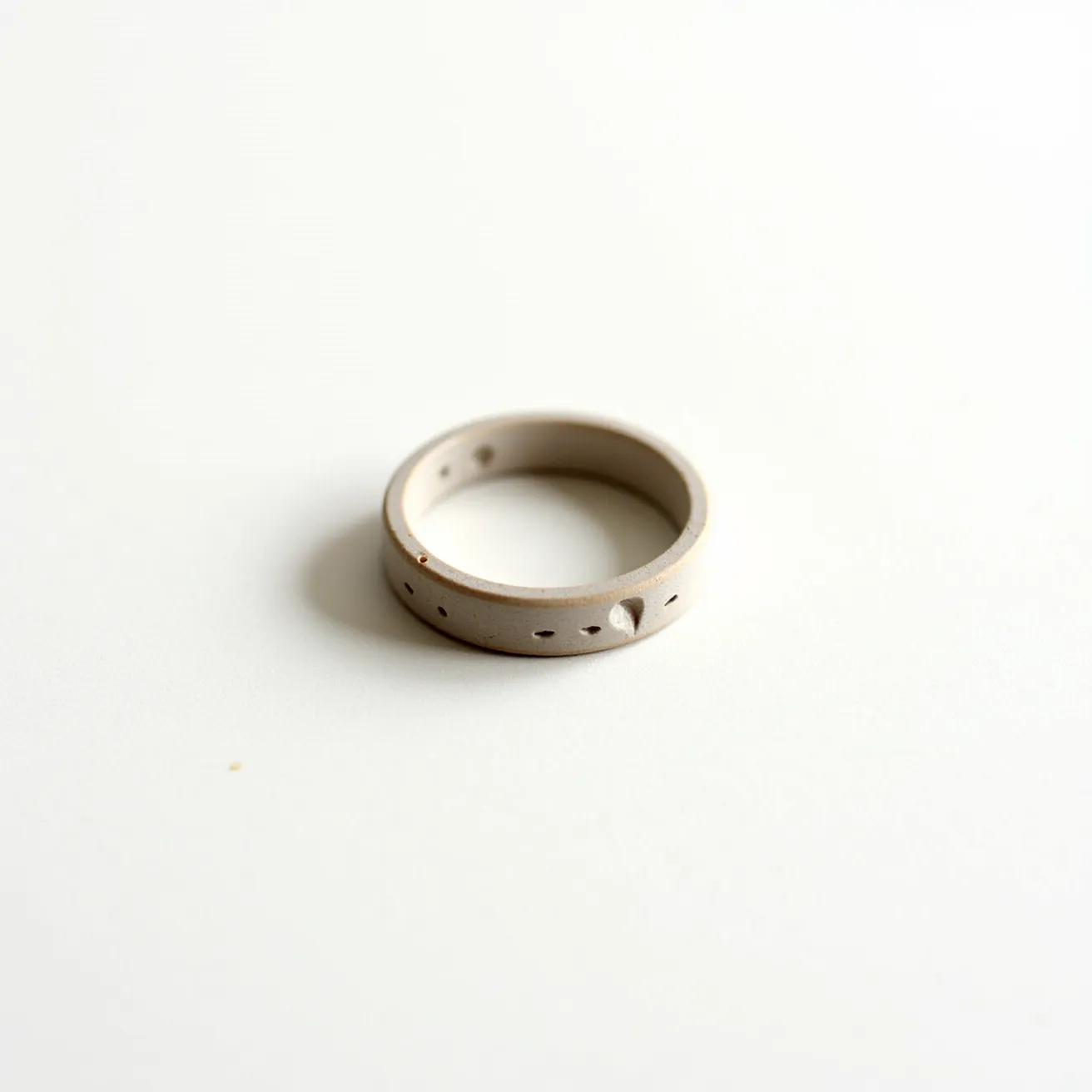 This groove ring is crafted from a matte, neutral-colored material, likely a type of metal or durable synthetic compound. The design features a smooth finish with evenly spaced, small groove-like indentations encircling its surface, creating a subtle yet distinctive pattern. There are no visible gems, stones, or detailed settings on the ring, as its appeal lies in the understated texture created by the grooves. The ring is a continuous band without any visible clasps or attachments, highlighting its simple and seamless construction.