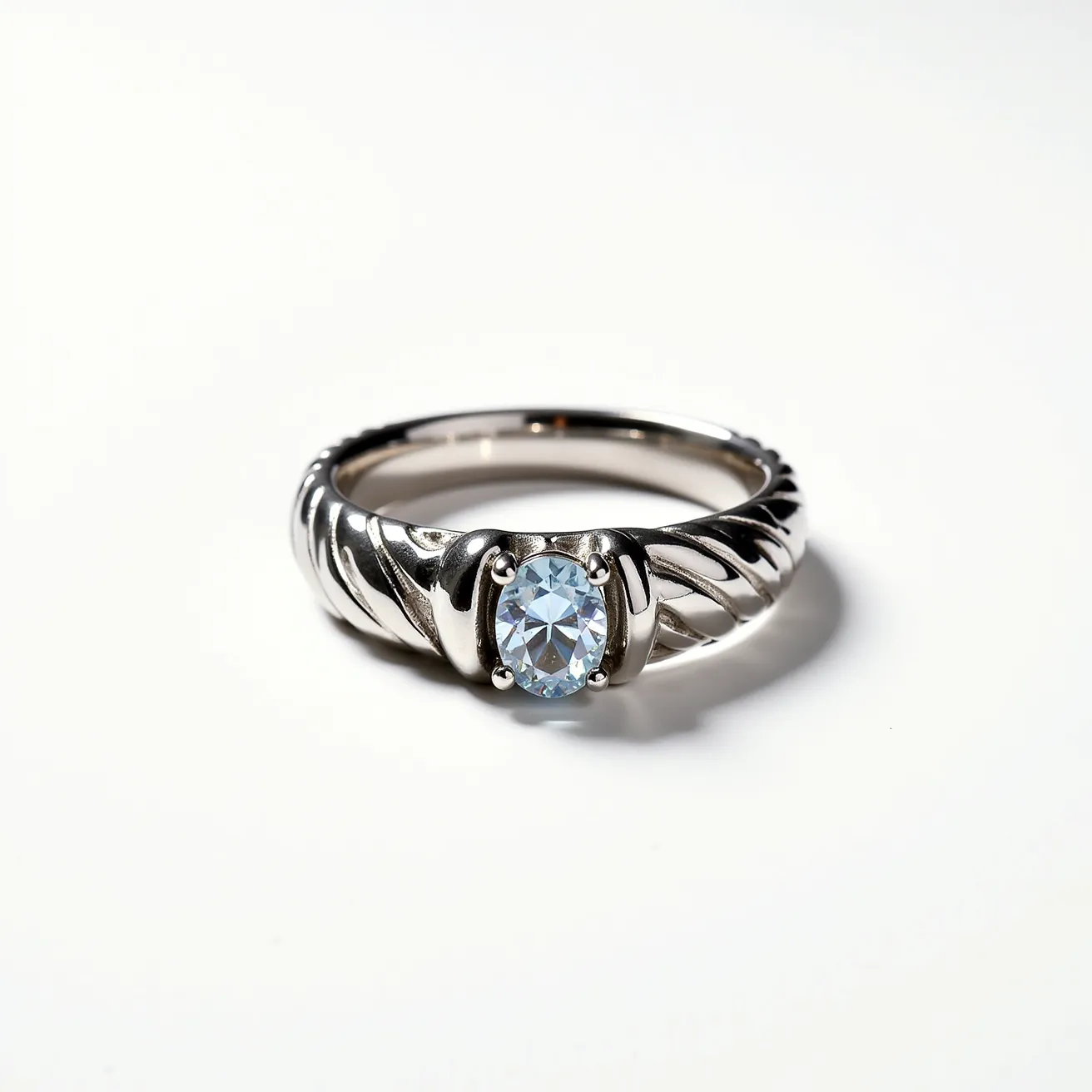 This groove ring features an intricate design crafted from a reflective metal, possibly white gold or platinum, showcasing a smooth, polished finish with elegant grooves along the band. At its center, the ring prominently displays an oval-cut gemstone that is clear in appearance, likely a diamond or similar stone, held securely in place by a classic four-prong setting, enhancing the stone's brilliance. The thoughtful design and high-quality materials combine to create a sophisticated and timeless piece of jewelry.