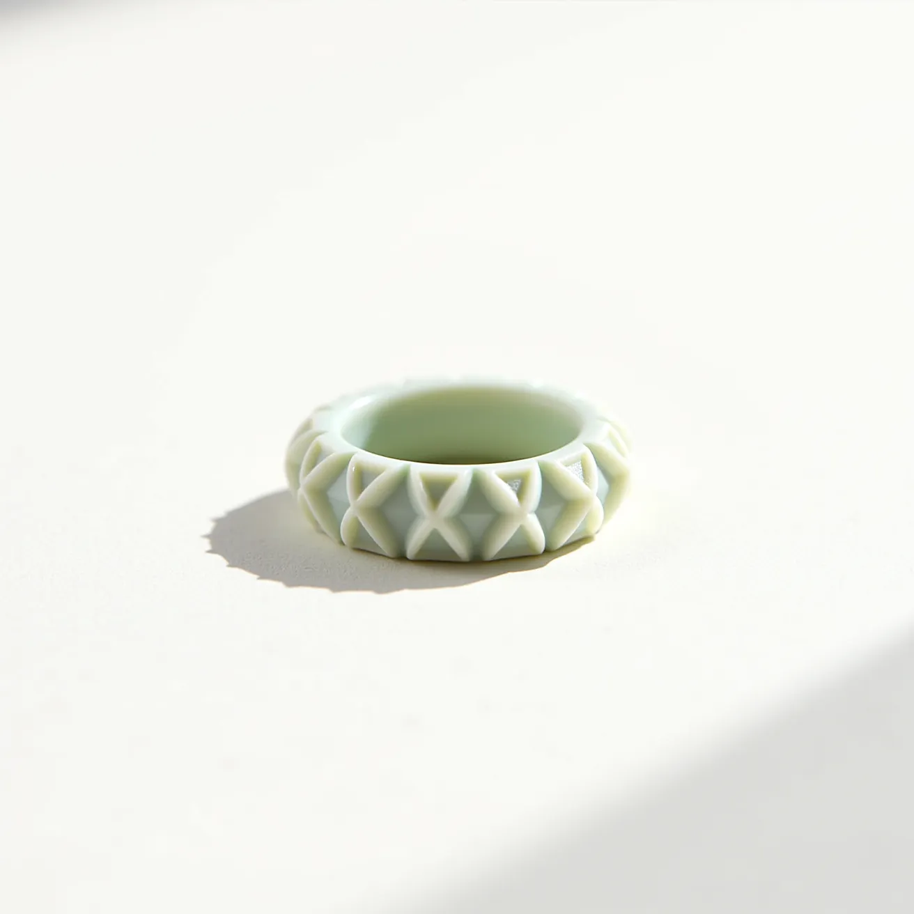 This groove ring features a textured exterior characterized by a series of raised, interlocking X-shaped patterns, crafted from a light green material that has a smooth, matte finish. The ring has a seamless, continuous band without any added gems, integration of stones, or settings. Its simple design gives it a modern and minimalist aesthetic, emphasizing the geometric groove patterns. The absence of a clasp or attachment indicates that the ring is designed to be slipped on the finger.