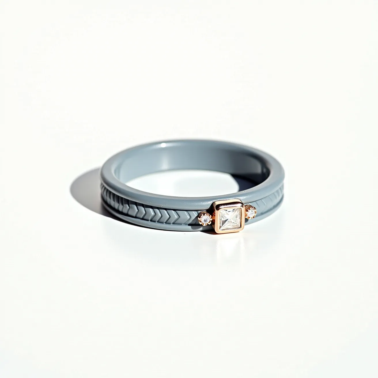 This groove ring features a sleek, modern design crafted from a smooth, gray silicone material. The ring is adorned with a square-cut gem set in a bezel setting, with two smaller round gems flanking it on either side. The central gem is framed in a golden metal, adding a touch of elegance and contrast to the utilitarian silicone band. The band itself displays a subtle pattern, contributing to the ring's textured aesthetic while maintaining a comfortable fit without any clasps or attachments.