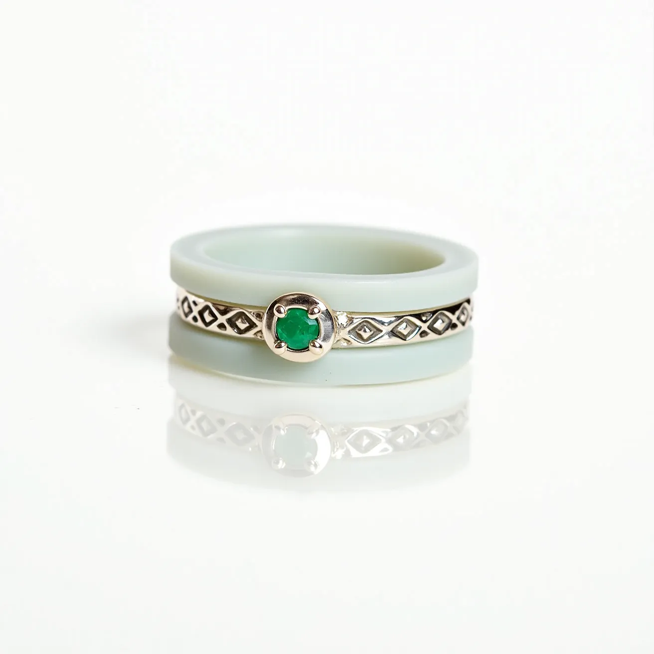 This groove ring features a two-part design with an outer band likely crafted from a smooth, soft material, possibly silicone or a lightweight metal, in a light color. The inner band showcases an intricate metallic design, possibly silver, with diamond-shaped cut-outs enhancing its aesthetic appeal. At the center, a round green gemstone is set prominently in a bezel setting, offering a vibrant contrast with its surrounding elements. The gemstone is carefully secured, emphasizing the ring's blend of simplicity and decorative detail. There is no visible clasp or attachment mechanism, indicating a continuous circular design for comfortable wear.