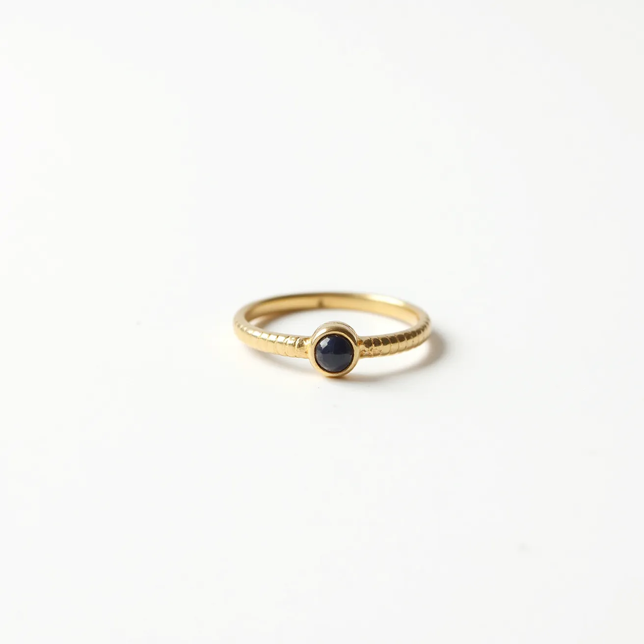 This groove ring features a sleek gold band with a textured finish, enhancing its elegant and understated design. At the center, it showcases a dark, smooth cabochon gem, likely a black onyx, set within a bezel setting that securely holds the stone in place while adding a subtle decorative element. The simplicity of the design is complemented by the continuous, unbroken circle of the band, which lacks any visible clasp or attachment, emphasizing its minimalist aesthetic.