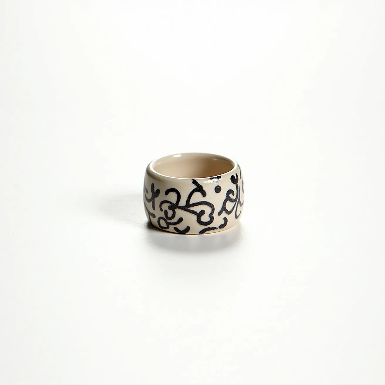 This groove ring features a smooth, wide band design primarily made from a material that mimics the appearance of ceramic or polished metal. It is adorned with dark, intricate, swirling patterns that give it an ornamental and artistic look. The ring lacks gemstones, showcasing instead these detailed engravings as its primary decorative element. The interior of the band is plain, exhibiting a polished finish. There is no visible clasp or attachment, suggesting a simple slip-on style suited for everyday wear.