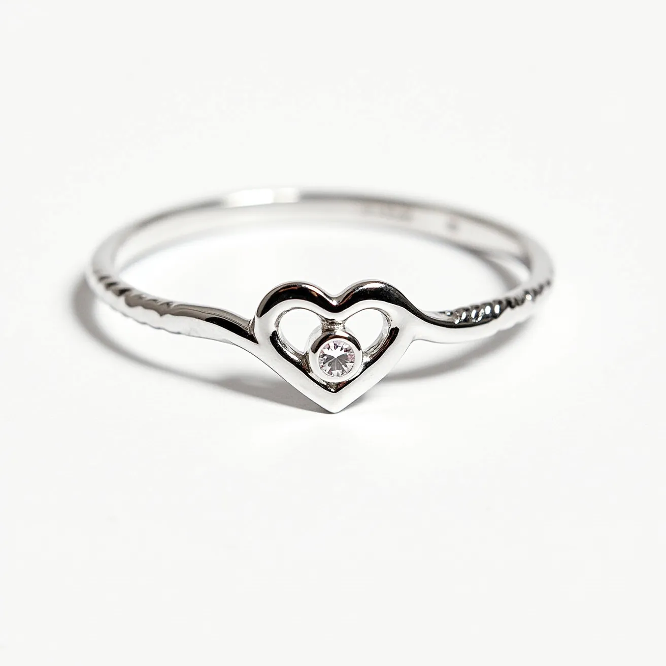 This heart promise ring features a delicate band crafted from polished metal, likely silver or white gold, with a minimalist design. At its center is an open heart shape, elegantly highlighting a round-cut gemstone, possibly a diamond or cubic zirconia, held securely in a bezel setting. The fine band is sleek and smooth, without any additional clasps or attachments, making the ring both graceful and simplistic in its form.