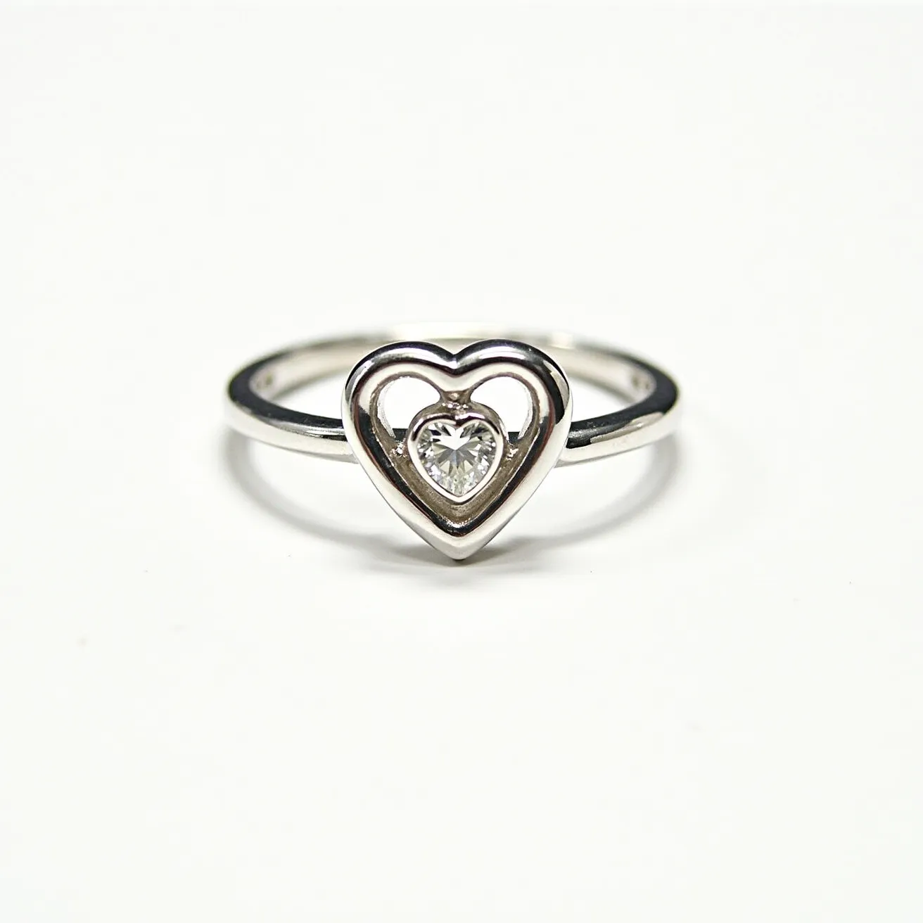 This heart ring features a sleek and polished metal band, likely made from white gold or platinum. At its center, a heart-shaped gem, potentially a diamond, is expertly cut and set within a hollow heart outline. The setting is secure, allowing the stone's brilliance to be on full display. The overall design is elegant and modern, combining the charm of the heart motif with the timeless allure of a sparkling gem. The ring seems to lack any additional clasps or attachments, highlighting its simplicity and refined craftsmanship.