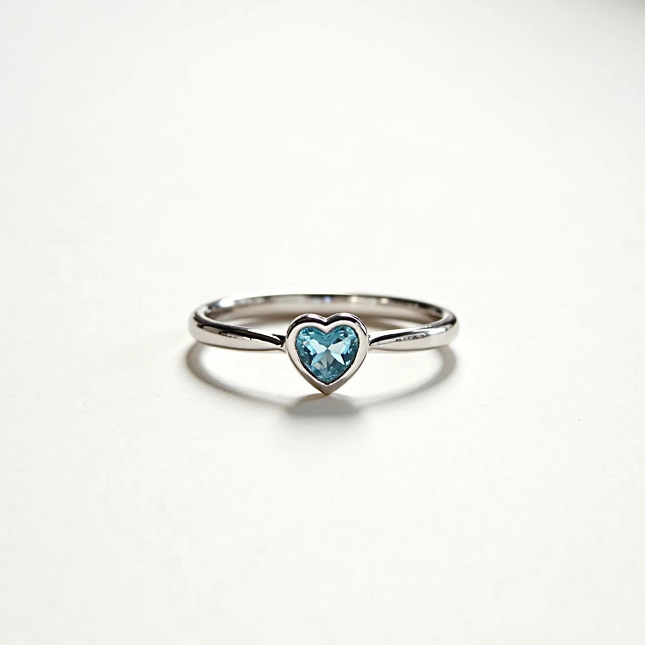 This heart ring features a sleek, polished band likely made of silver or white gold, giving it a lustrous shine. The centerpiece is a heart-shaped blue gemstone, possibly a blue topaz or aquamarine, expertly cut and securely set in a bezel setting that frames the gem's shape. The setting ensures the stone is well-protected while also highlighting its delicate hue. There are no visible clasps or attachments, indicating a traditional closed-circle design for the band.