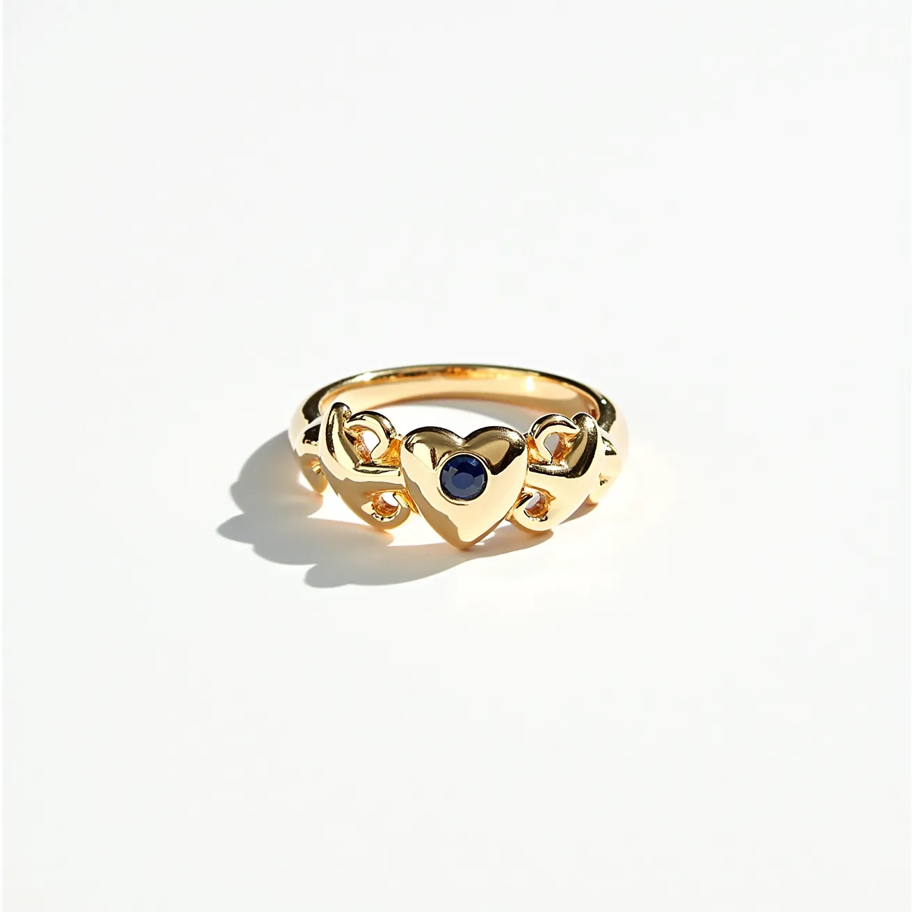 This heart ring features a delicate gold band adorned with intertwined heart motifs. At the center of the prominent heart motif, a round, deep blue stone is set, likely a sapphire, which adds a striking contrast to the gold. The gem is bezel-set, providing a secure and elegant finish. The overall design showcases a timeless and romantic charm, with the intertwining hearts enhancing the continuous loop of the band. The ring exudes a sense of elegance suitable for both everyday wear and special occasions.