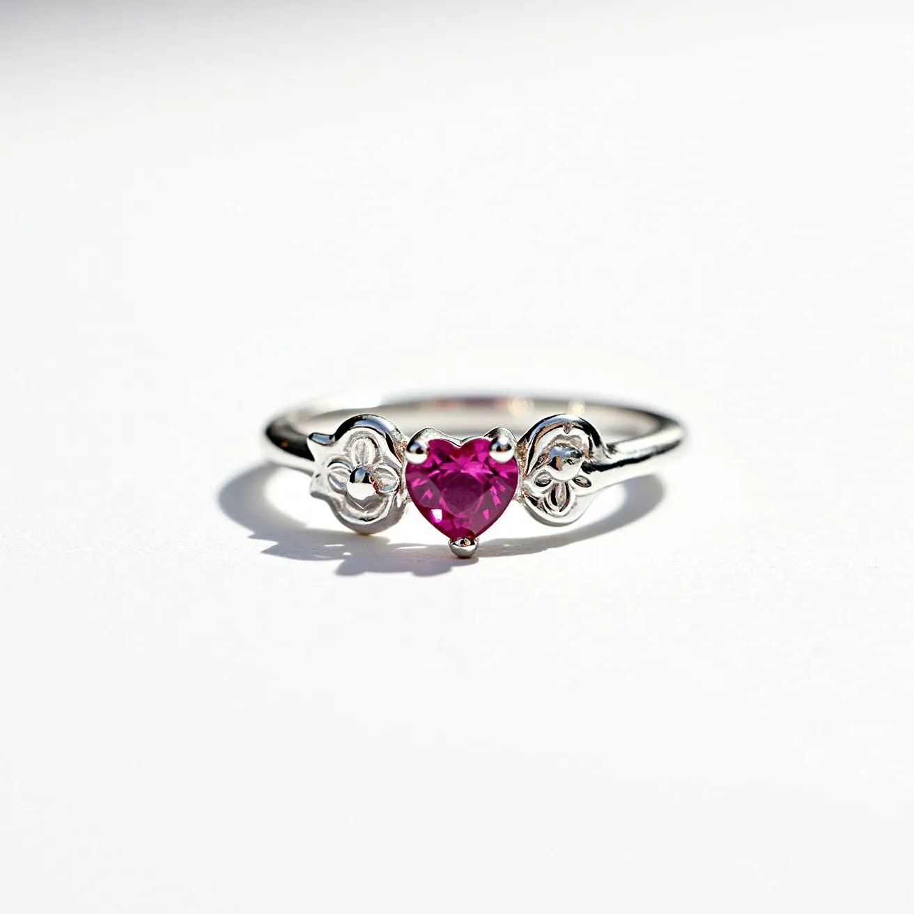 This heart ring features a delicate design crafted from silver-toned metal, providing a sleek and elegant appearance. At its center, a vibrant pink heart-shaped gemstone is prominently displayed, skillfully cut to enhance its brilliance and draw attention. This gemstone is held in place with a prong setting, ensuring stability while allowing maximum light to pass through, enhancing its sparkle. Flanking the central stone are intricately detailed floral motifs, adding a touch of sophistication and charm to the overall design. The band itself is slender, complementing the refined aesthetic and maintaining focus on the central gemstone.