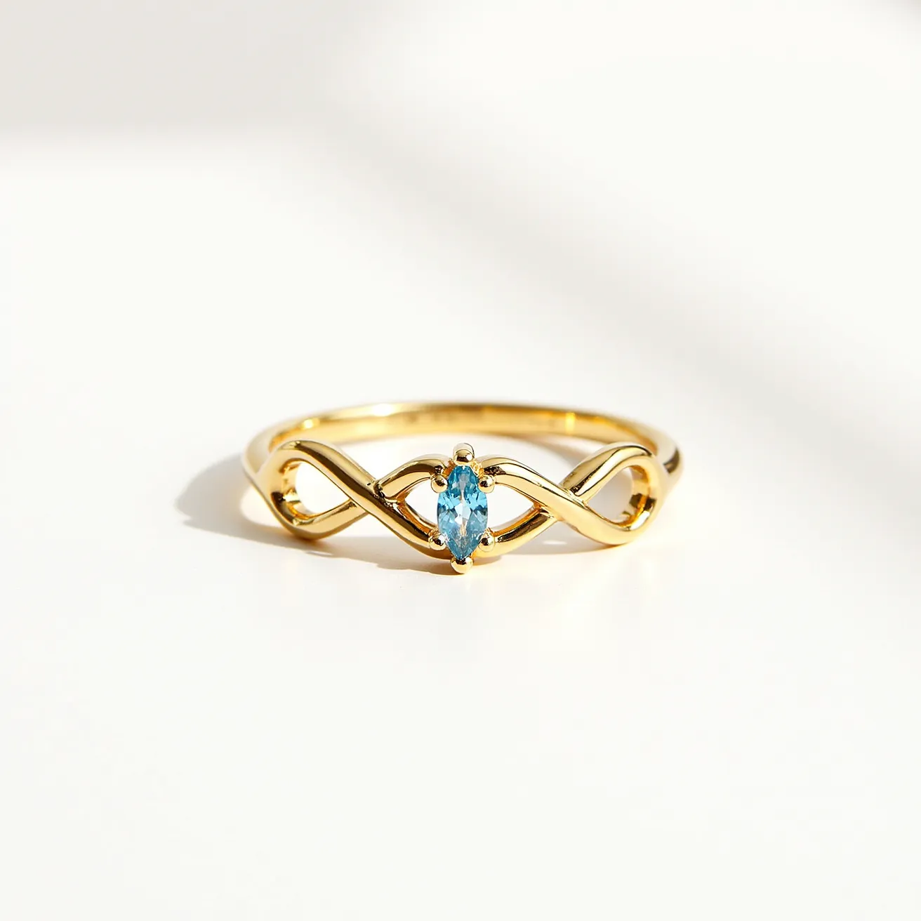 This heart ring features a gold band with an elegant intertwining design. At its center is a striking marquise-cut blue gemstone, set in a prong setting, which securely holds the stone in position. The design combines the warmth of the gold with the coolness of the blue gem, creating a balanced and sophisticated aesthetic. There is no visible clasp or attachment, as the band is continuous and smooth, emphasizing the delicate flow of the intertwined motifs.