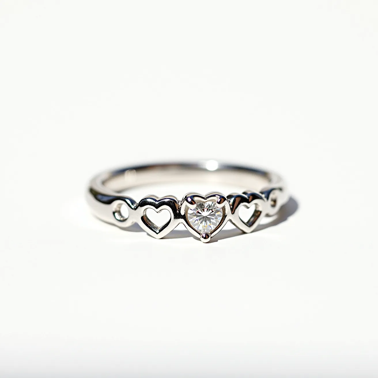 This heart wedding ring features a charming design crafted from a shiny metal, possibly white gold or platinum, with a polished finish. The ring is adorned with interconnected heart-shaped cutouts encircling the band, each symbolizing love and unity. At its center, a heart-shaped diamond is beautifully set in a prong setting, allowing the gemstone to capture and reflect light brilliantly. The simple elegance of the ring’s style is enhanced by the precise arrangement of the hearts and the central stone, offering a timeless and romantic appeal.