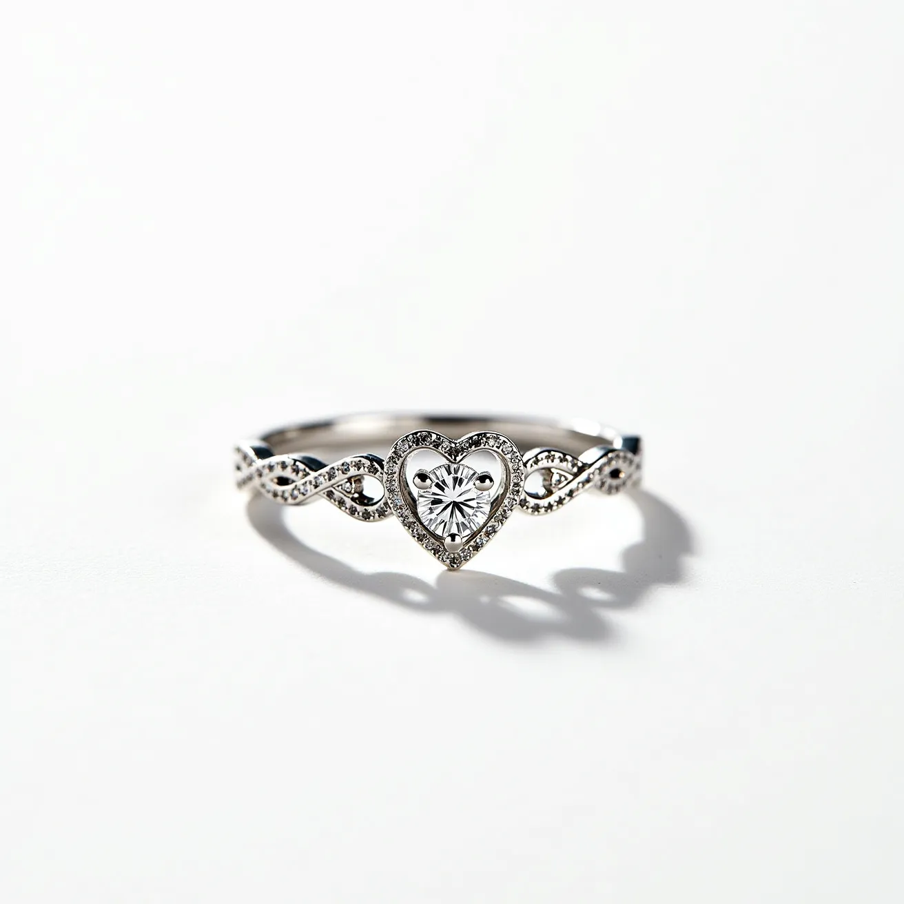 This heart wedding ring showcases a central heart-shaped gemstone, likely a diamond, secured in a bezel setting. The gleaming metal appears to be a high-quality silver or white gold, providing an elegant backdrop for the central stone. Surrounding the heart-shaped gem, a series of small, round-cut diamonds adorn the band in an intricate infinity or filigree pattern, enhancing the ring's romantic and timeless appeal. The continuity of the ring's design is seamless, with no visible clasp or attachment, highlighting its delicate craftsmanship and attention to detail.