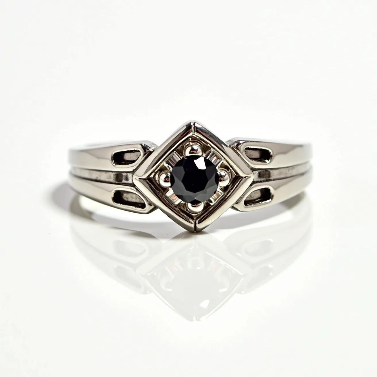 This hematite ring features a polished, black hematite stone at its center, cut in a round, faceted style to enhance its reflective qualities. The stone is securely set within a metal band that exhibits a geometric design, accentuating the modern aesthetic of the piece. The band appears to be crafted from a silver-toned metal, complementing the dark luster of the hematite. The setting includes small prongs that elegantly hold the stone in place, while the band showcases cut-out details that add a touch of sophistication and uniqueness to the overall design.