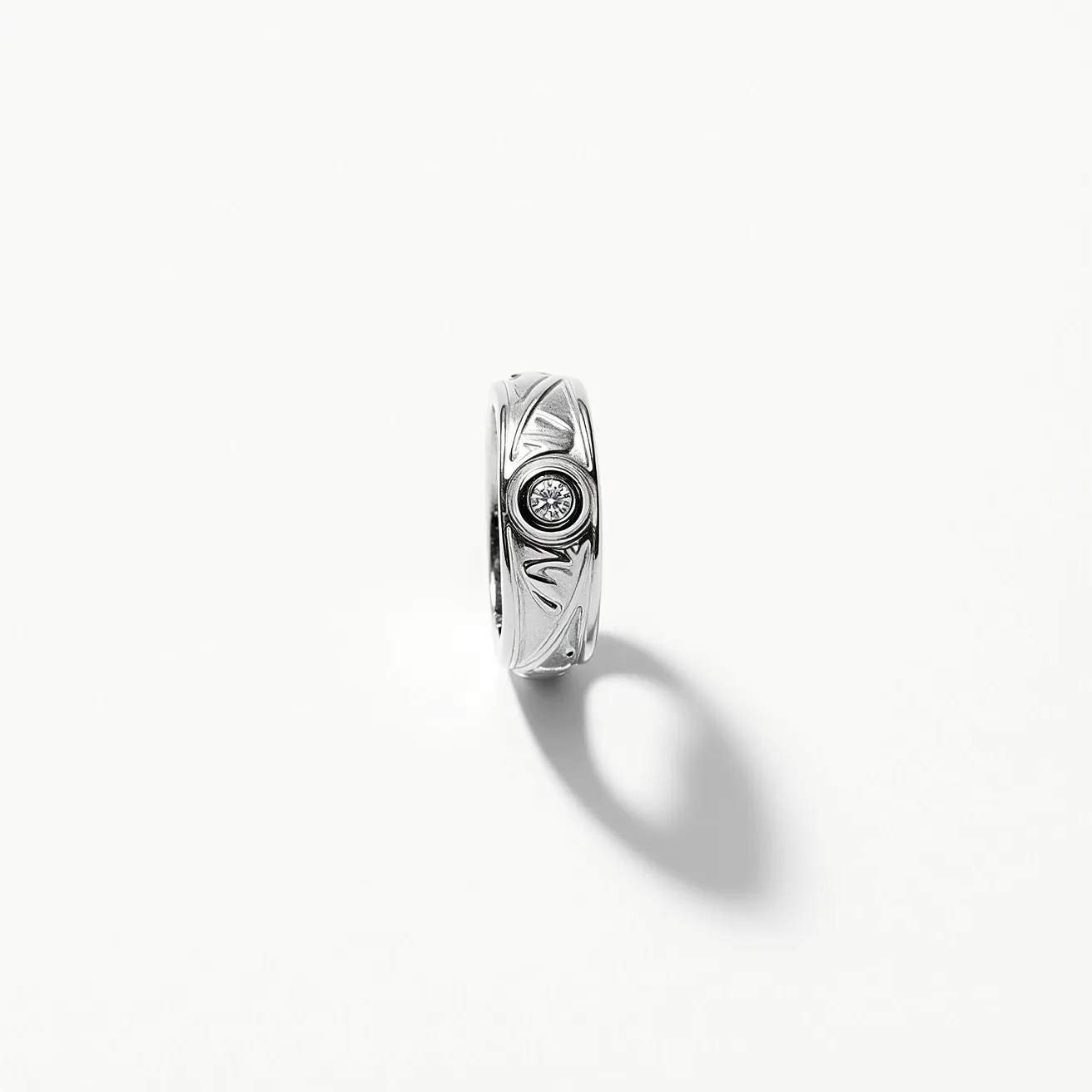 This hematite ring is crafted with a polished, metallic finish, featuring a sleek and modern design. The band displays a delicately etched pattern that enhances its visual appeal. At the center of the ring is a single, round gemstone, possibly a diamond, presented in a bezel setting, which securely encases the gem while allowing its brilliance to be showcased effectively. The overall design is both elegant and understated, combining the reflective quality of hematite with the sparkle of the central stone.