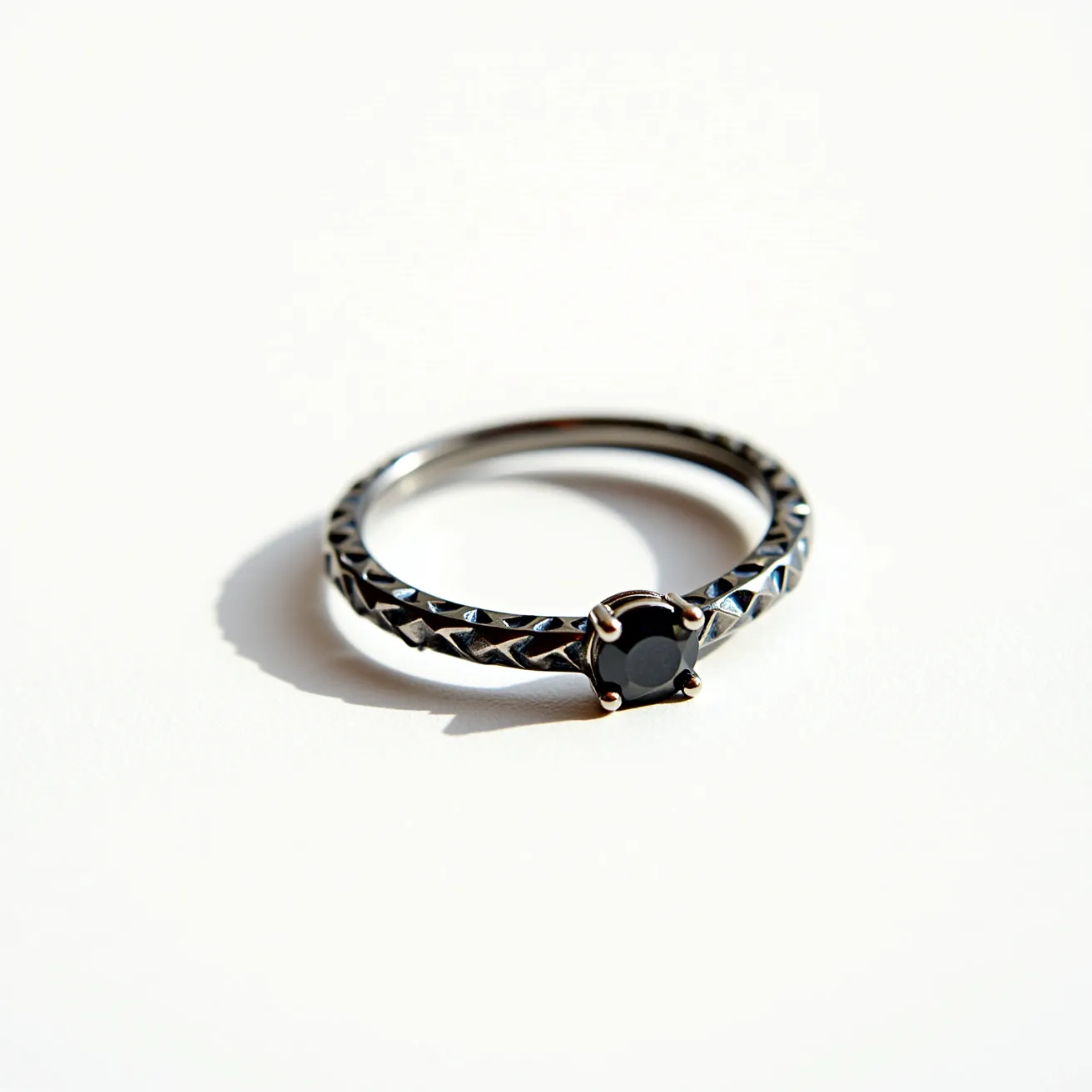 This hematite ring features a smooth, metallic sheen characteristic of hematite, with a striking dark polish that gives it a sophisticated allure. The band is intricately designed with a textured pattern that enhances its visual appeal, suggesting a meticulous crafting process. At the center is a round-cut gemstone, also likely hematite, held securely in place by a four-prong setting made of a complementary metal. The prongs add a touch of elegance while ensuring the gemstone's stability and prominence on the ring. There are no visible clasps or attachments, indicating it is a traditional ring design meant to be worn on the finger.