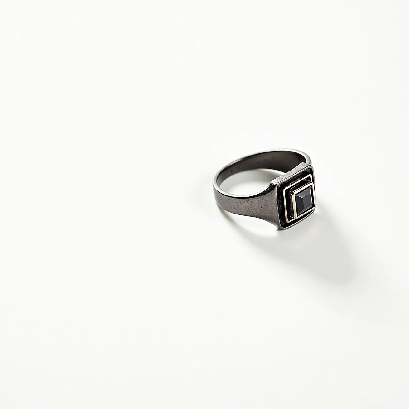 This hematite ring features a sleek band crafted from a metallic material, showcasing a central square-cut stone that appears to be made of hematite, known for its reflective shine and dark coloration. The stone is set into a geometric design with a dual layered frame that adds dimension and modernity to the piece. The setting appears to be secure, likely adopting a bezel or similar design that frames the stone elegantly. There is no additional clasp or attachment, as the ring is a simple, continuous band, emphasizing its minimalist and contemporary aesthetic.