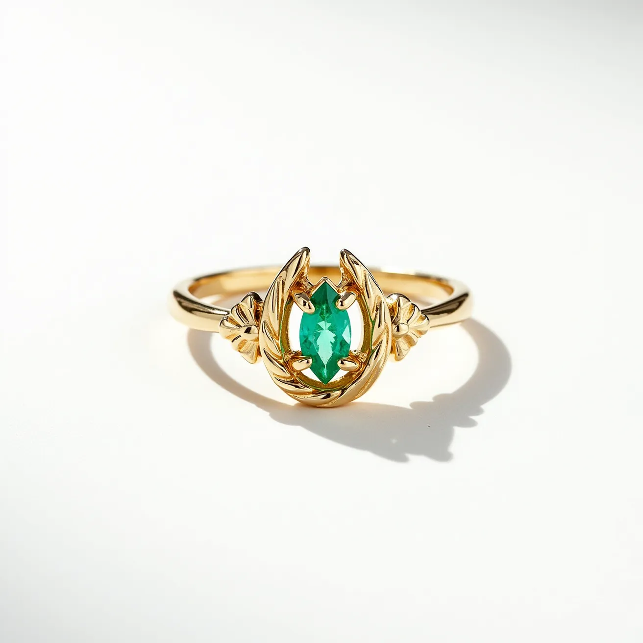 This horseshoe ring features a delicate gold band that elegantly forms the shape of a horseshoe at the top. Centrally set within the horseshoe is a vibrant, green, marquise-cut stone, likely an emerald, which is securely held in place by four prongs. The intricate design of the setting is enhanced by leaf-like detailing on either side of the gem, adding a touch of nature-inspired elegance to the piece. The ring does not require any clasp, as it is a typical band style that slides onto the finger.