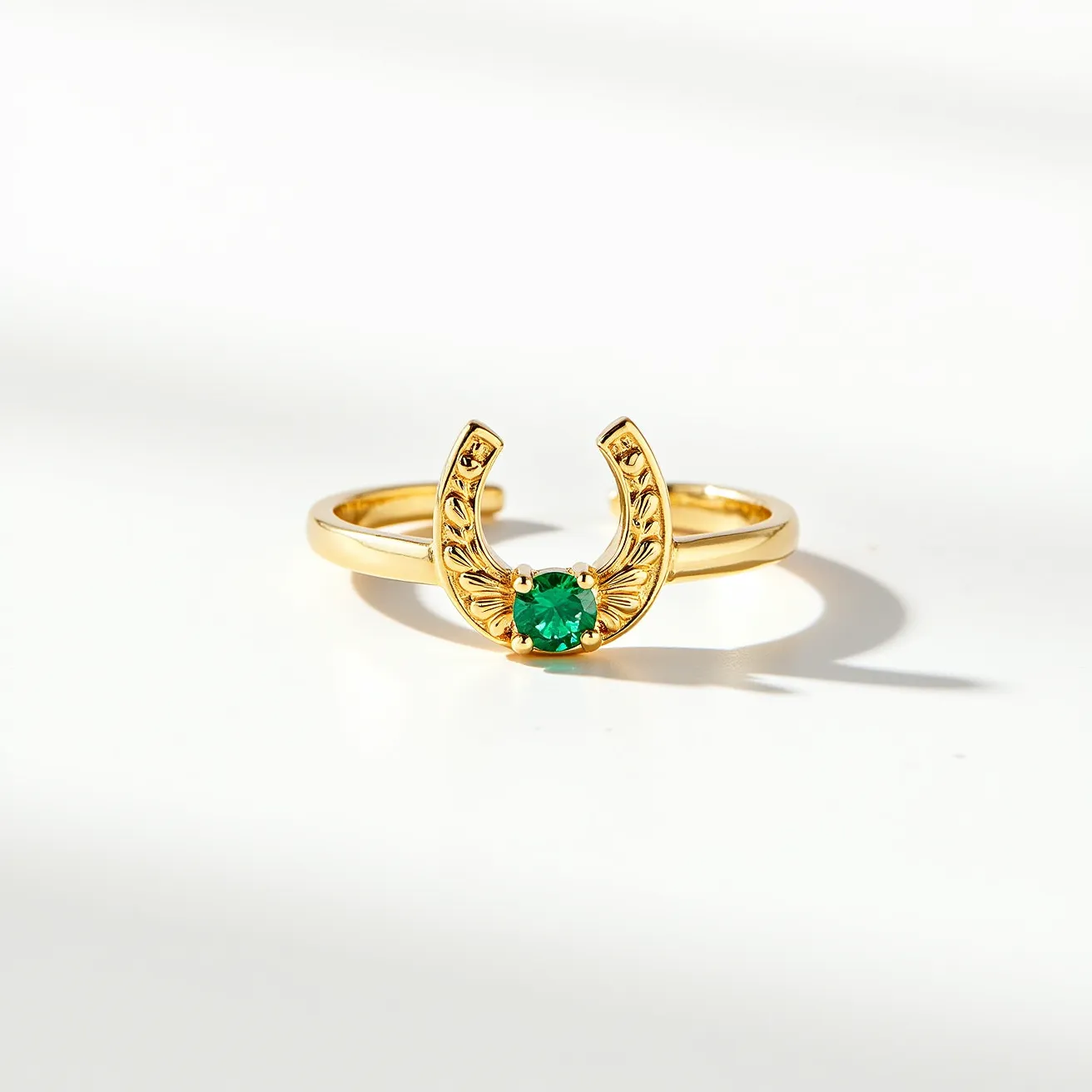 This horseshoe ring is crafted from a gold material, featuring a striking design highlighted by an intricately engraved horseshoe motif. At the center, it showcases a vibrant round-cut green gem, likely an emerald, that is securely set in a classic prong setting. The elegant simplicity of the gold band allows the detailed horseshoe and central gemstone to take prominence, creating a harmonious balance between the materials and design elements. The open-ended horseshoe serves as the focal point, accentuating the stylish and symbolic nature of the ring.