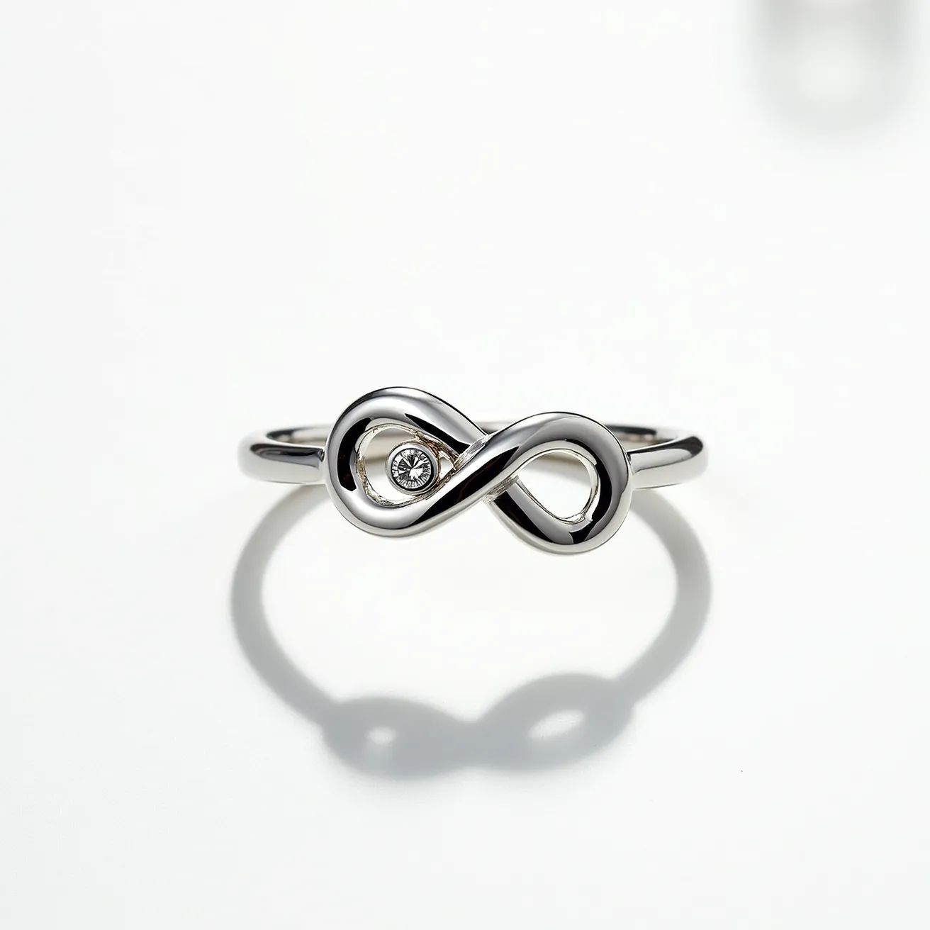 This infinity ring is crafted from a polished silver or white gold band, featuring a sleek and smooth infinity symbol as its centerpiece. Within one loop of the symbol, a small, round diamond or similar gemstone is set, likely in a bezel setting, providing a subtle, elegant sparkle. The gemstone is securely encased, enhancing the ring's seamless design while ensuring durability and comfort in wear. The overall style of the ring is minimalist yet thoughtfully designed, focusing on the timeless infinity motif.