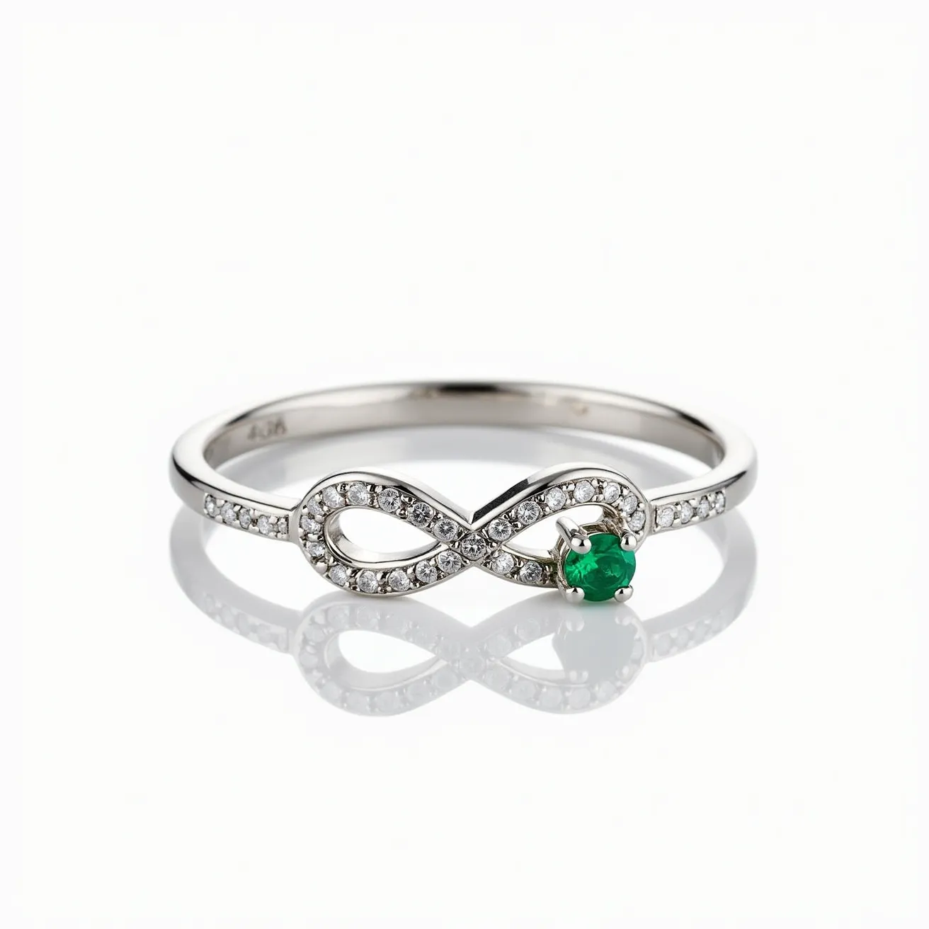 This Irish promise ring features a sleek band crafted from polished white metal, likely silver or white gold. The centerpiece is an elegant infinity symbol encrusted with small, round-cut white stones, possibly diamonds or cubic zirconia, set in a pavé style that adds delicate shimmer. A vibrant green gemstone, likely an emerald, is prominently displayed in a prong setting at the heart of the infinity symbol, adding a touch of color and significance. The ring's design is symbolic and intricate, embodying themes of eternity and commitment.