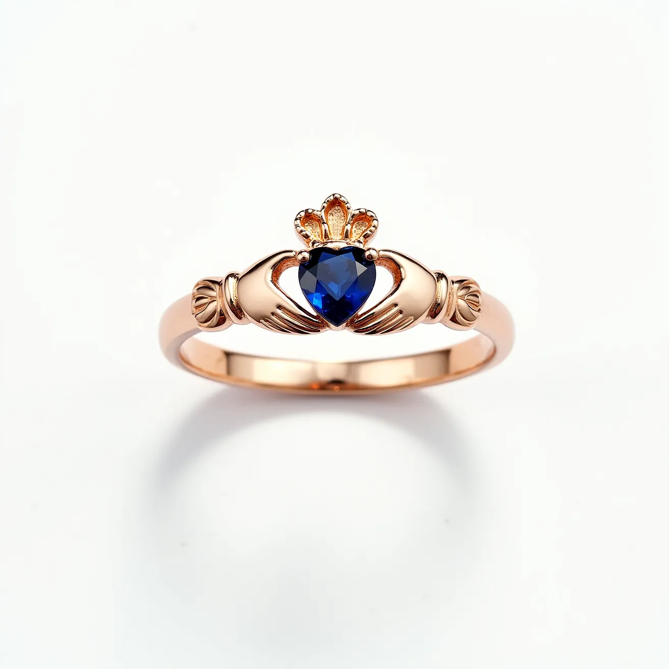 This Irish promise ring is crafted from a warm, rose gold metal and features a classic Claddagh design, symbolizing love, loyalty, and friendship. At the center of the design is a heart-shaped blue sapphire, expertly cut and set into a secure bezel. The hands cradling the heart add a meaningful touch, while a crown sits elegantly above the heart-shaped stone, signifying loyalty. The ring's band is smooth, enhancing the overall elegance and symbolism of the piece.