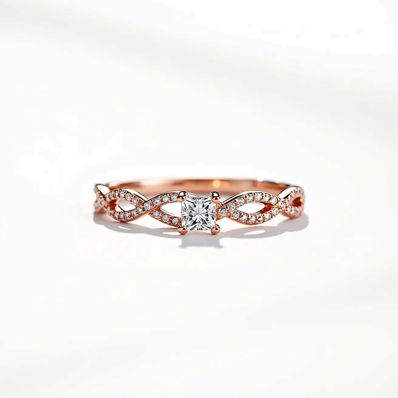 This Irish promise ring features a delicate design crafted from rose gold, showcasing an intertwined band adorned with small, pavé-set accent gems that enhance its elegance. The central feature is a square-cut stone, held securely in a four-prong setting, adding a stunning focal point that captures and reflects light beautifully. The ring's intricate detailing symbolizes unity and commitment, making it a meaningful and traditional piece.