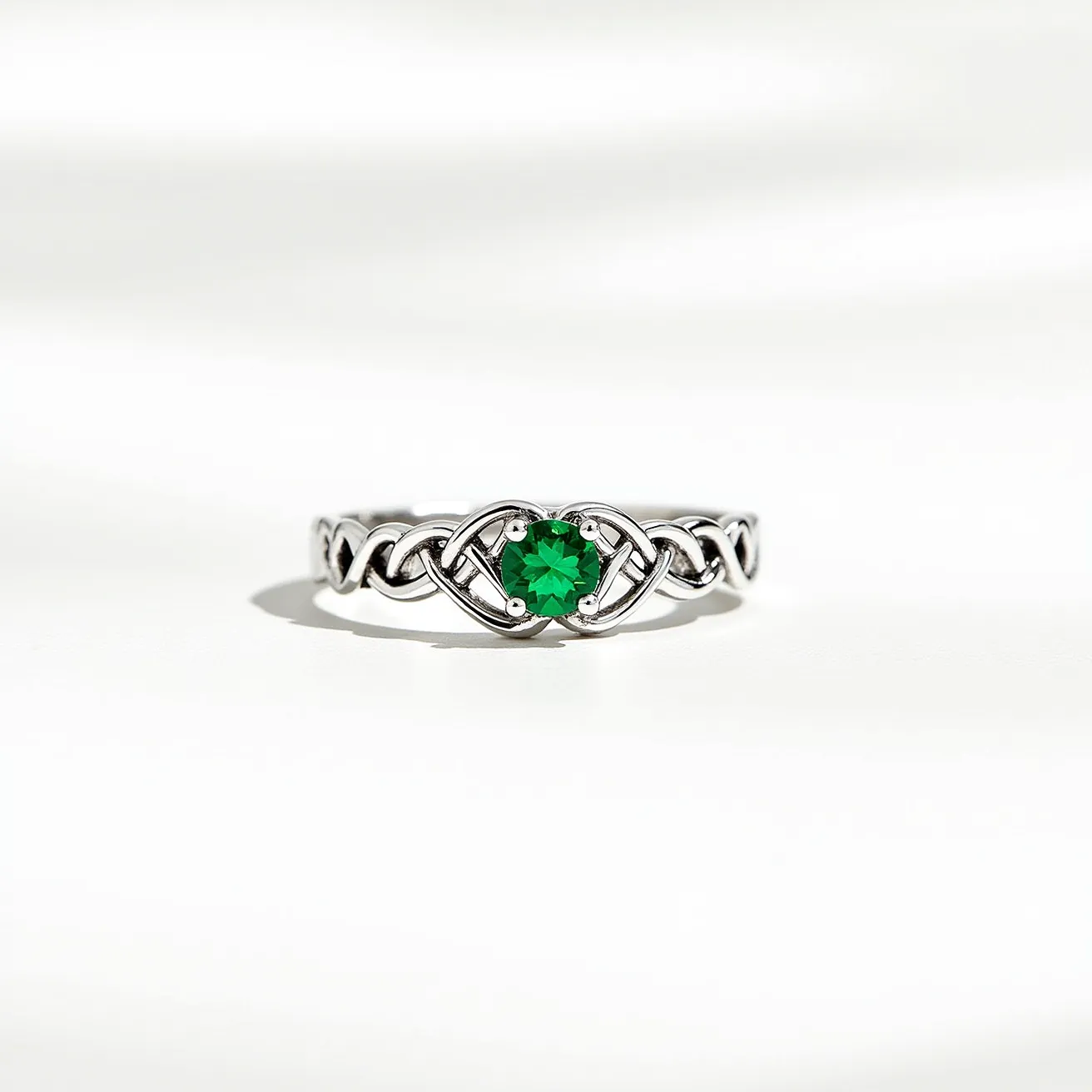 This Irish promise ring features a beautifully intricate Celtic knot design in silver, encircling a vibrant green gemstone at its center. The green gem, possibly an emerald or a similarly colored stone, is round-cut, adding a sparkling focal point to the piece. It is set in a secure prong setting, allowing the light to accentuate its color and brilliance. The silver band's detailed interlaced design symbolizes unity and eternity, making it a meaningful symbol for a promise ring. There is no visible clasp, as the ring is a continuous band designed for a snug, comfortable fit on the finger.