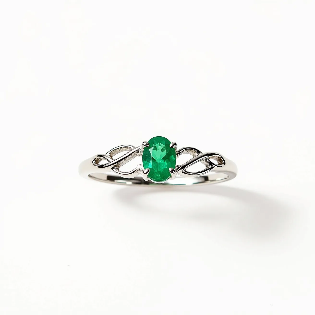 This Irish promise ring features a beautifully polished metal band, likely made of sterling silver or white gold, intricately designed with Celtic knot motifs that elegantly flank the central gemstone. The focal point of the ring is an oval-cut green stone, reminiscent of an emerald, set securely in a four-prong setting that accentuates its vibrant hue. The flowing design on the band complements the stone's elegance, embodying a sense of continuity and eternity symbolized by the Celtic patterns.