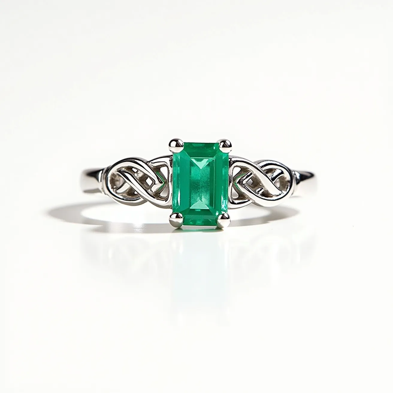 This Irish promise ring showcases a stunning emerald-cut green gemstone centrally set, likely representing an emerald, held securely by a four-prong setting. The band is crafted from a shiny metal, possibly sterling silver or white gold, and features elegant Celtic knot designs flanking the gemstone, symbolizing eternal love and commitment. The overall design is both intricate and meaningful, highlighting the cultural significance of Irish craftsmanship in jewelry.