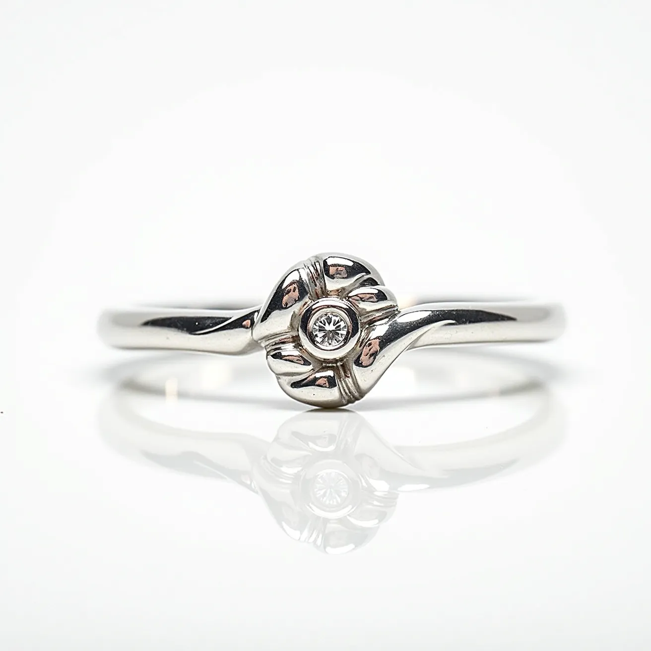 This knot ring is crafted from a polished metal, likely silver or white gold, featuring an elegant knot design at its center. The centerpiece of the knot holds a small, round-cut gemstone, possibly a diamond, set securely in a bezel setting which adds a subtle sparkle without overwhelming the delicate design. The band is smooth and narrow, complementing the refined craftsmanship of the knot. The lack of additional attachments or clasps ensures a seamless and graceful profile, emphasizing the simplicity and sophistication of the ring's design.