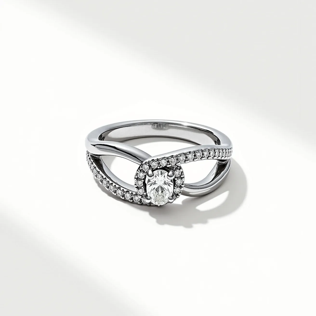 This knot ring is crafted from a polished metal, likely white gold or platinum, giving it a sleek and reflective appearance. It features a prominent oval-cut central stone, set in a secure prong setting that highlights its brilliance. Encircling this central stone is a delicate halo of smaller, round-cut stones, adding extra sparkle and intricacy to the design. The band incorporates a unique knotted style, with a split shank adorned with more of the same small stones, emphasizing elegance and symmetry. The overall design combines fluid lines with a touch of glamour, making it a stunning and sophisticated piece.